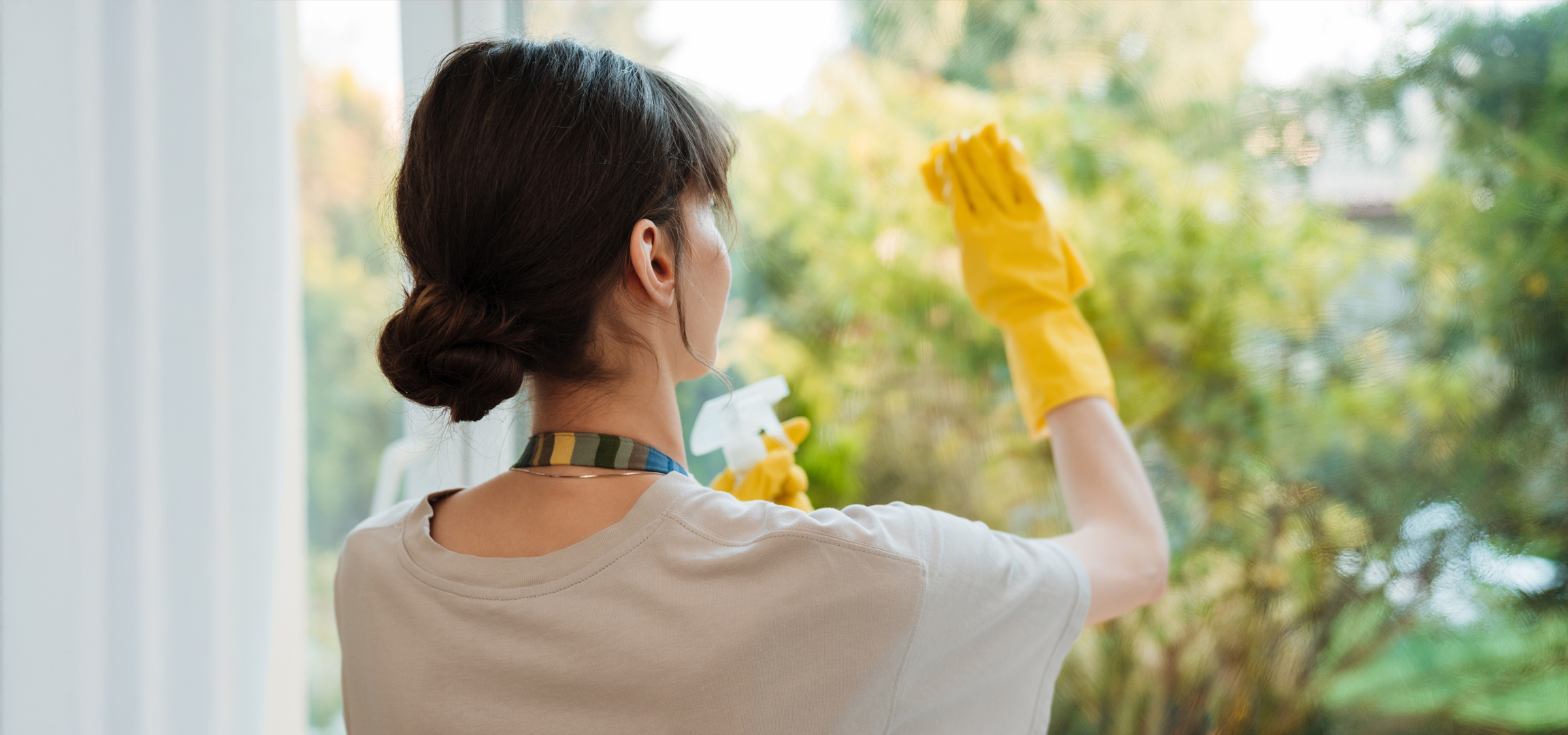 Nő tisztítja az ablakot sárga kesztyűben és ablaktisztítóval