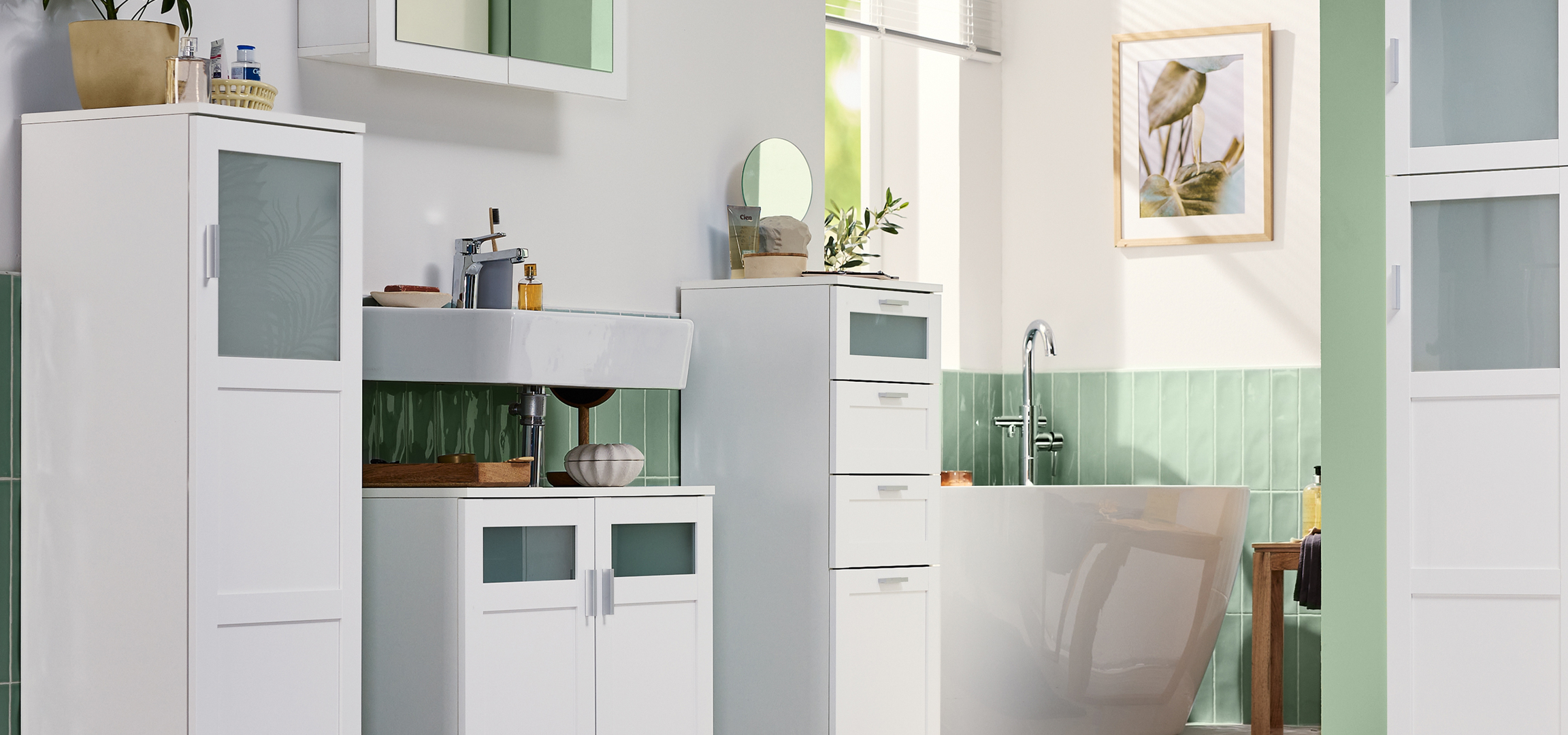 Fehér fürdőszobabútorok, mosdókagyló és zöld csempe egy modern fürdőszobában.