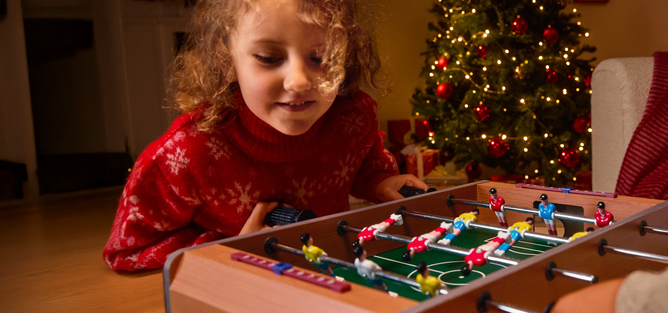 Gyerekek játszanak csocsóval karácsonykor, háttérben karácsonyfa.