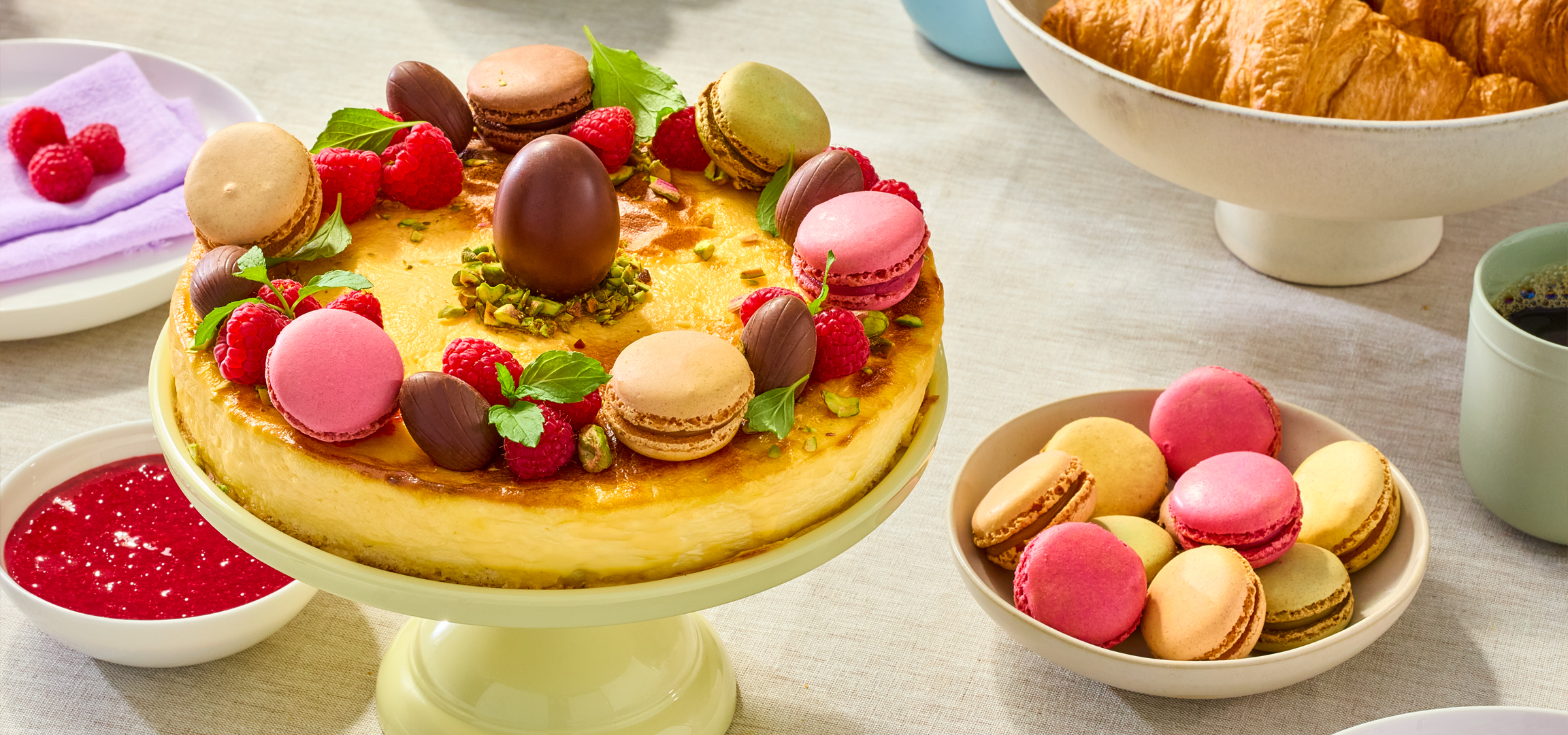 Sajttorta macaronokkal, málnával és csokitojásokkal, croissant-okkal és kávéval.