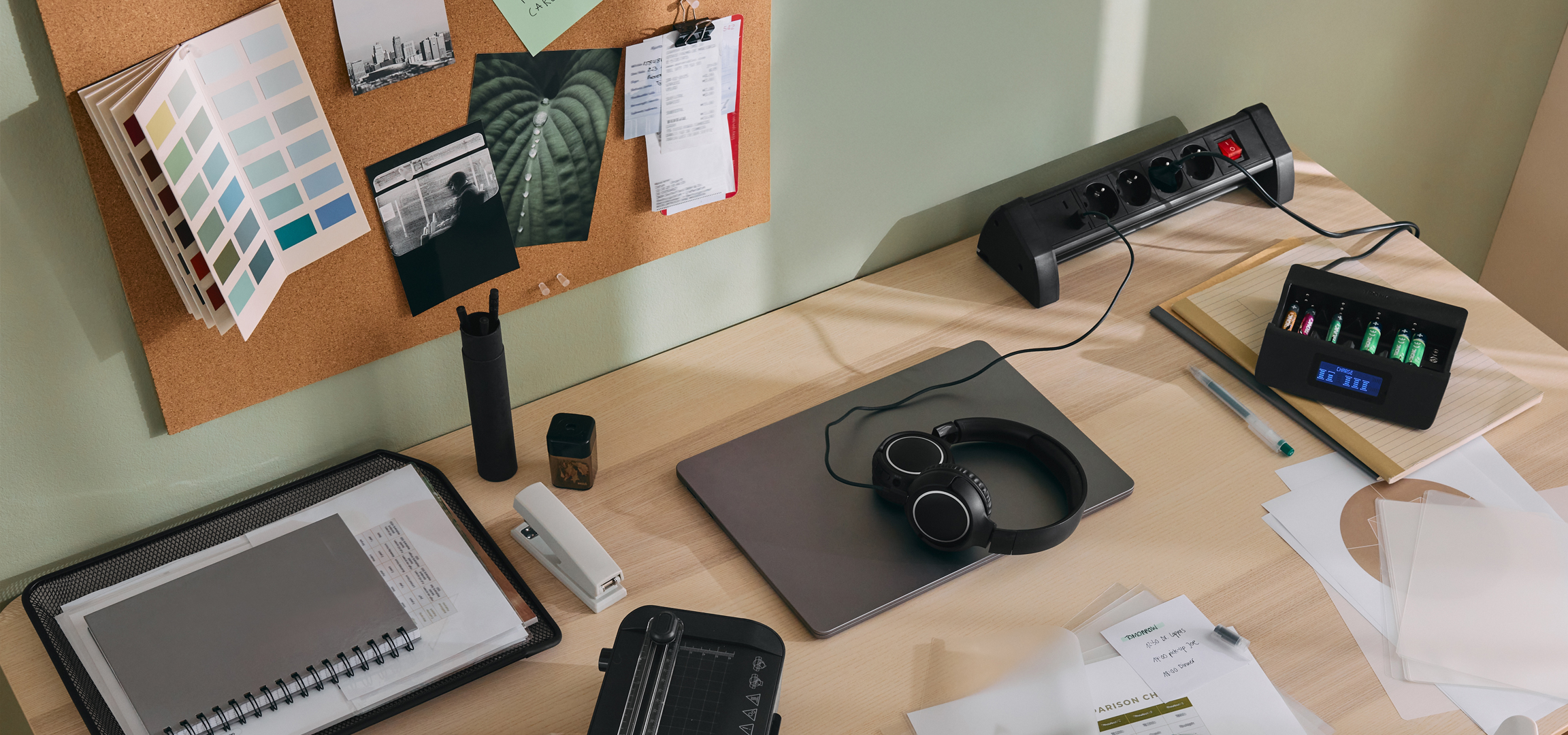 Íróasztal elosztóval, akkumulátortöltővel és parafatáblával, rajta színmintákkal és képekkel.