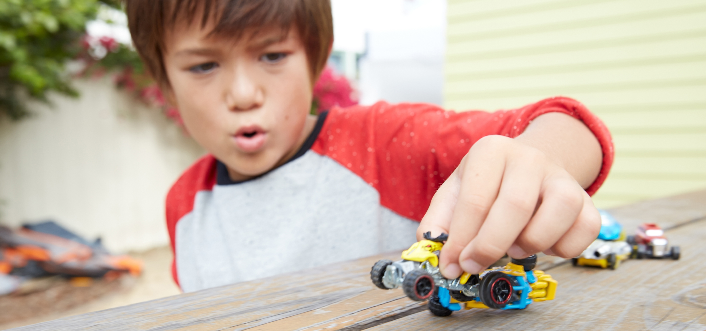 Fiú játszik játékautókkal egy fa asztalon.