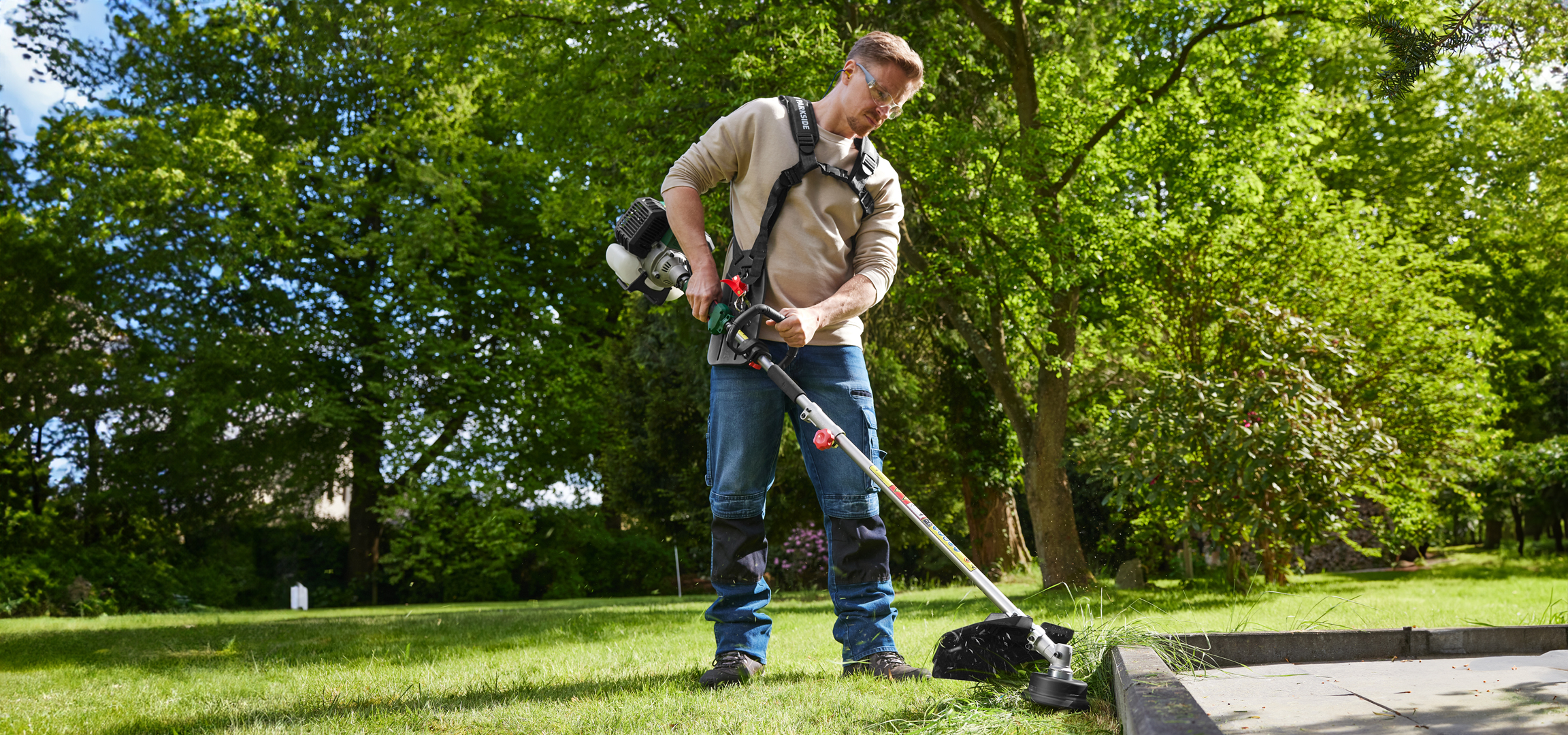 Férfi fűkaszával vágja a füvet egy napsütéses napon.
