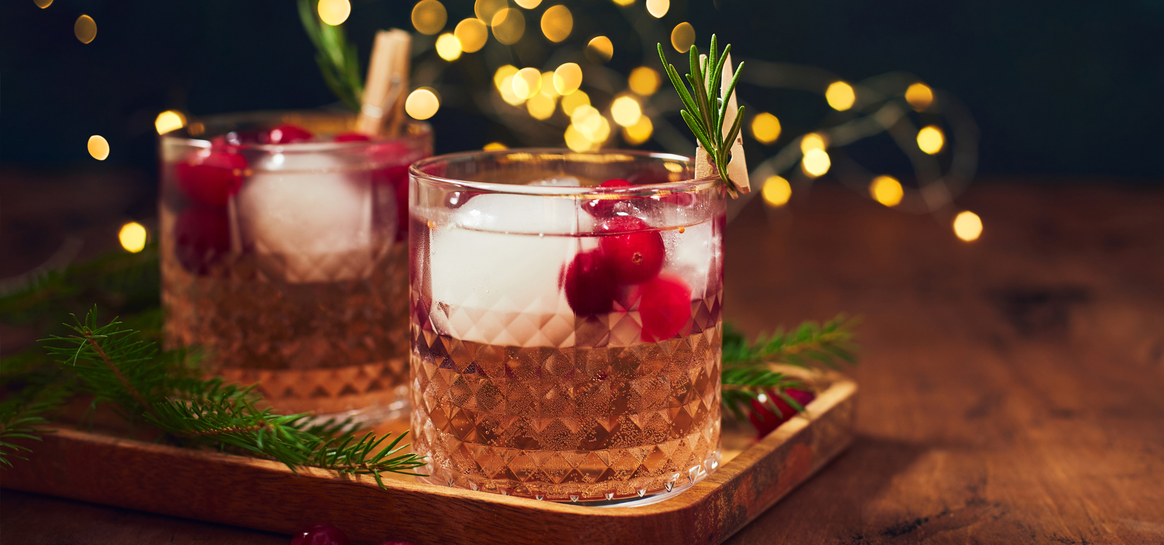 Ünnepi koktélok áfonyával és rozmaringgal, karácsonyi fényekkel és fenyőágakkal díszítve.