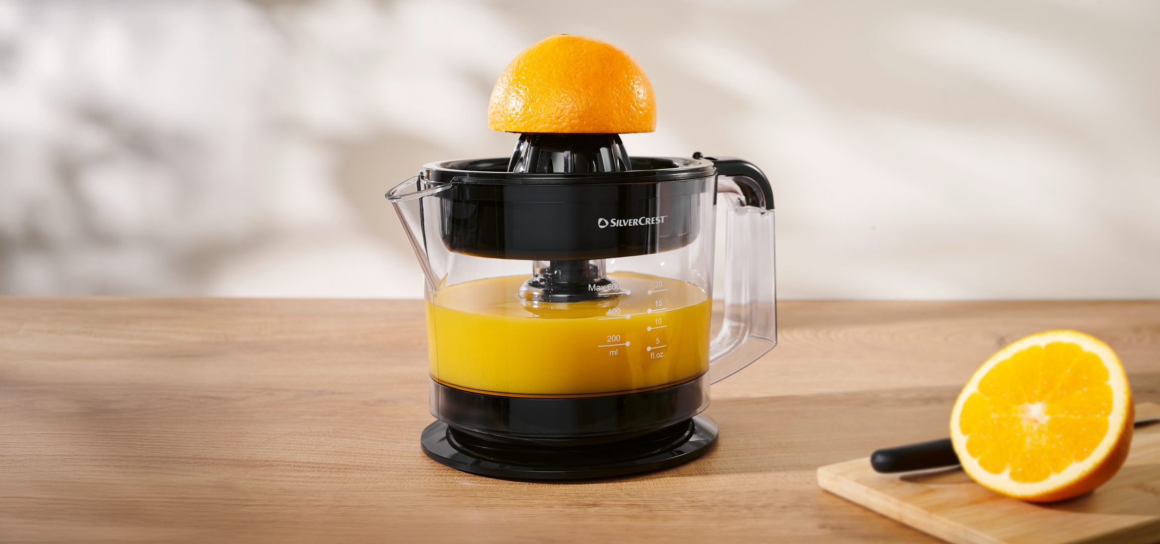 Silvercrest citrusprés narancslével és egy félbevágott narancs vágódeszkán
