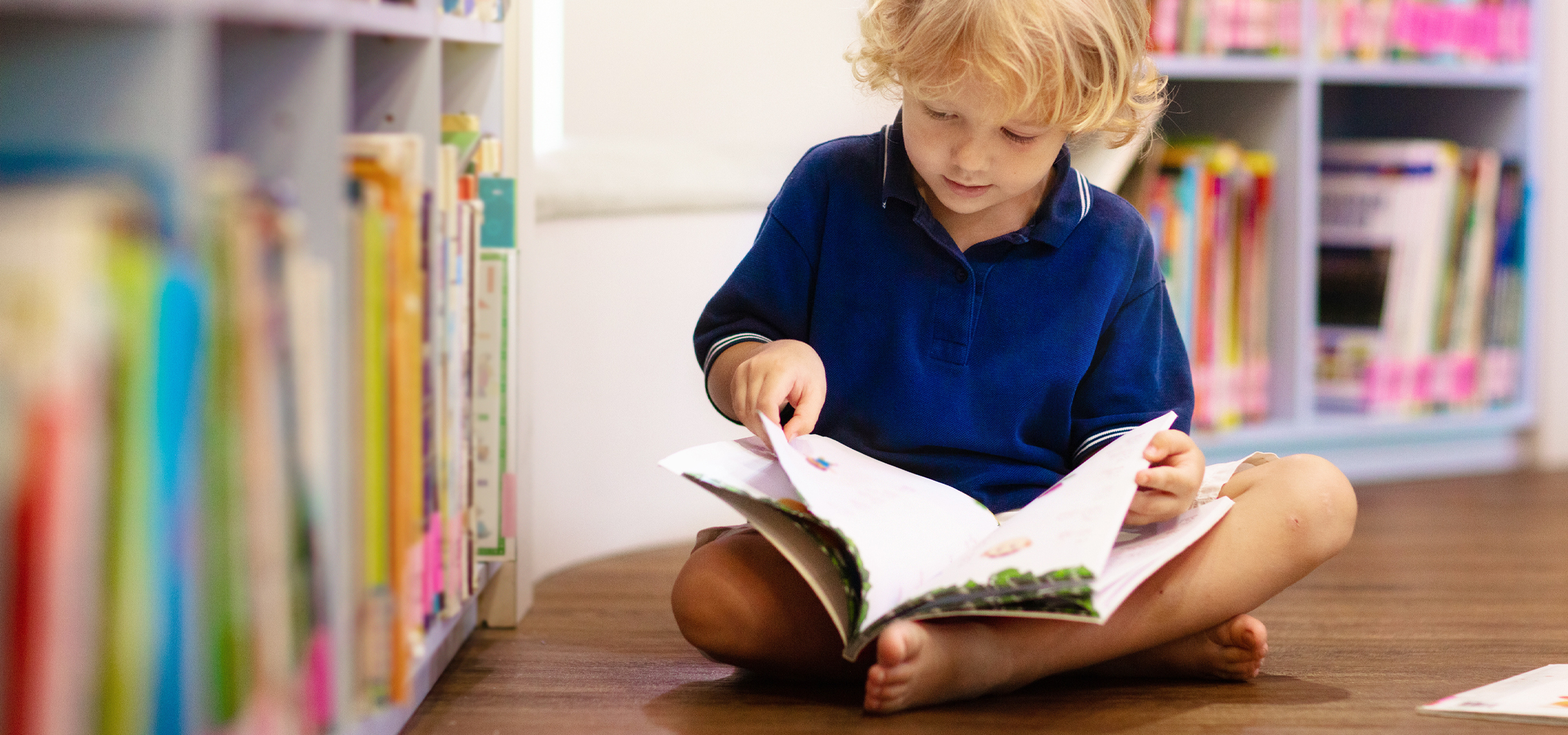 Egy kisfiú olvas egy könyvet a könyvtárban, színes könyvekkel a háttérben.
