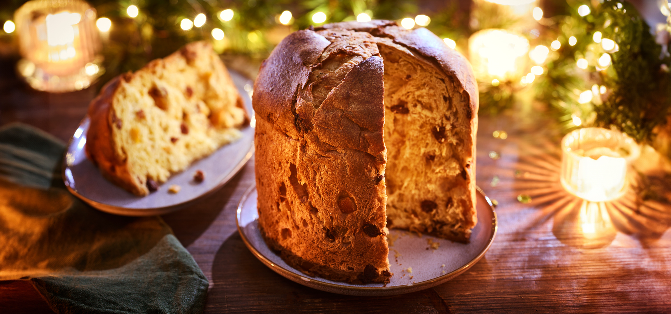 Panettone szelettel, karácsonyi dekorációval és gyertyákkal egy fa asztalon.