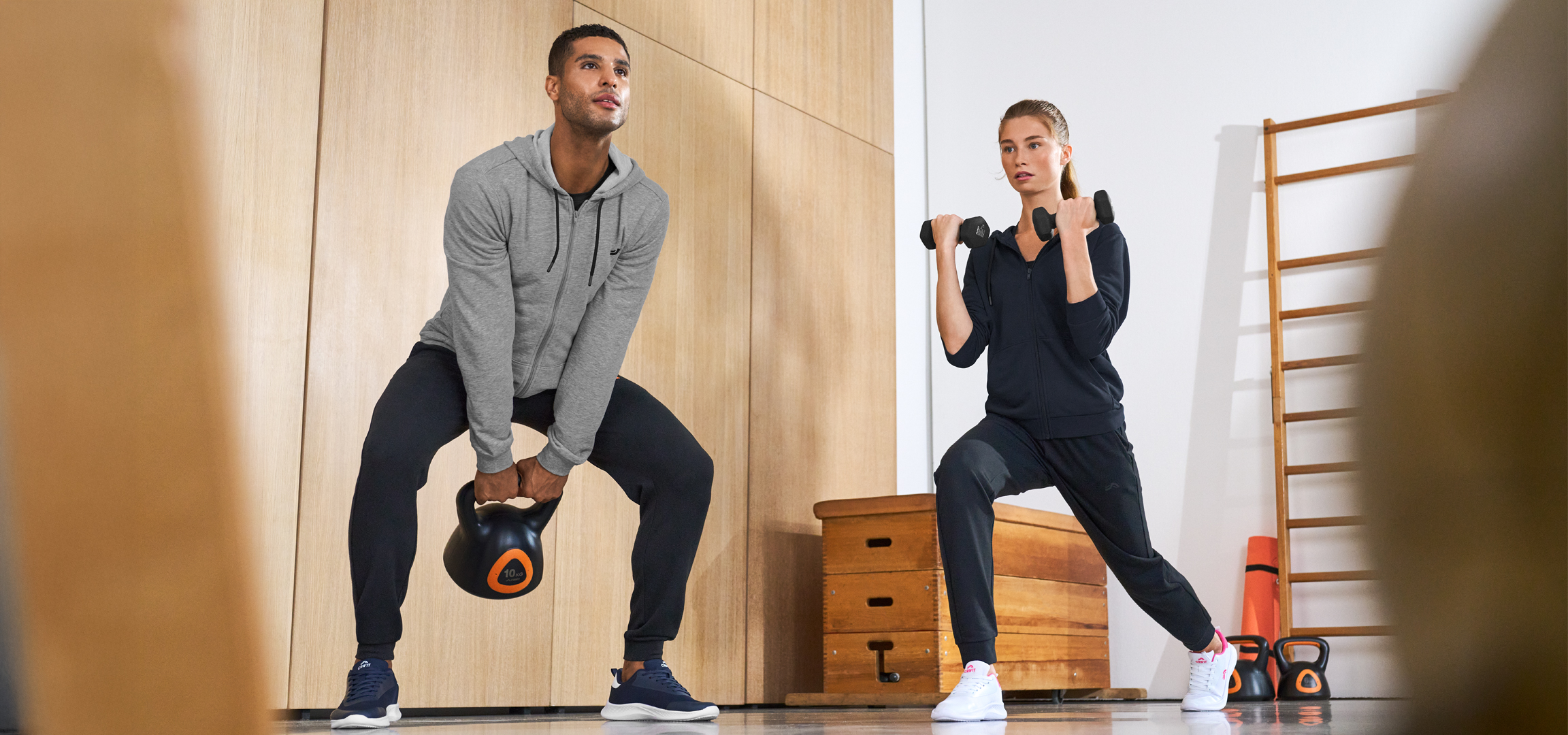 Férfi kettlebellel, nő súlyzókkal edz egy edzőteremben.