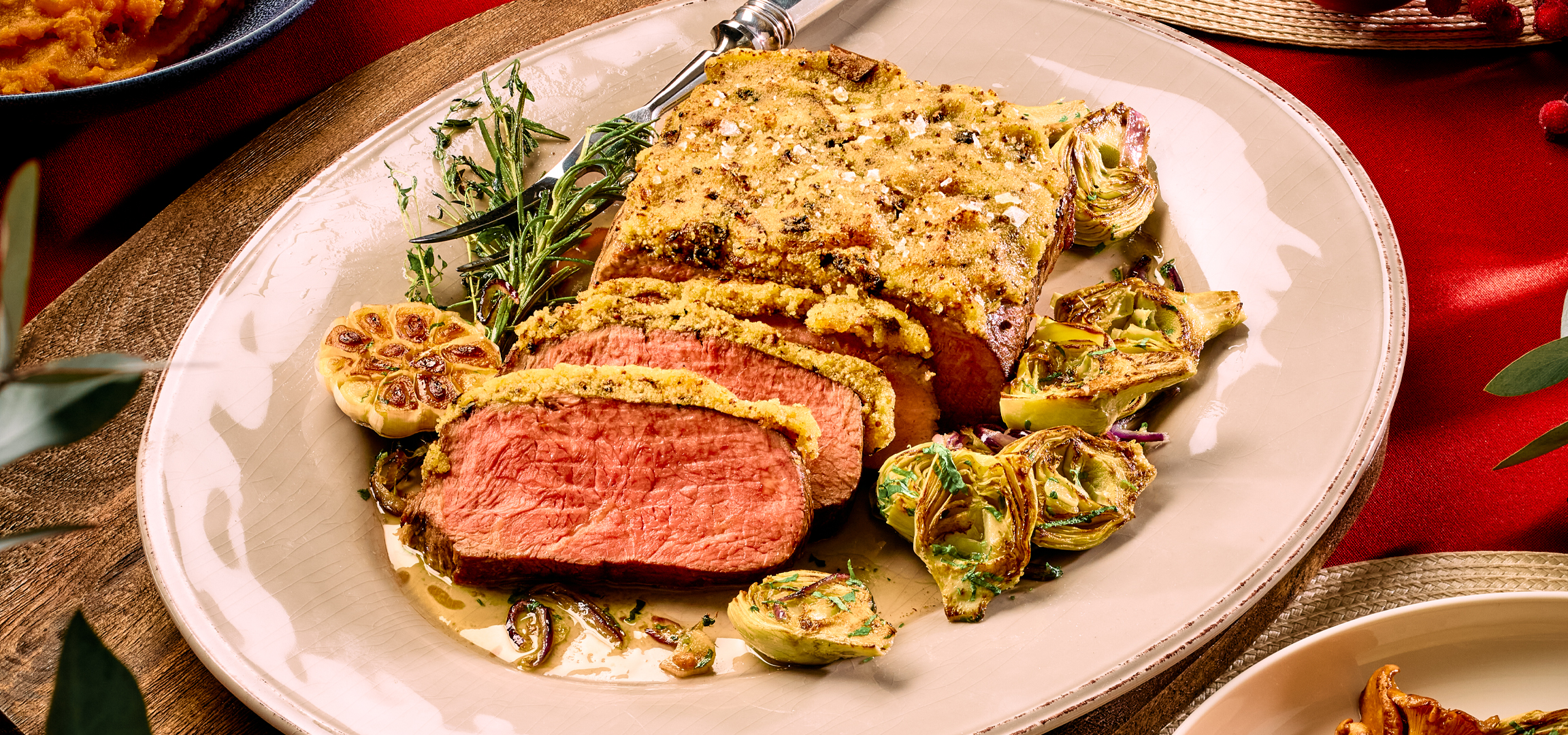 Sült hús, burgonyapüré és sült burgonya egy asztalon, zöld levelekkel díszítve.