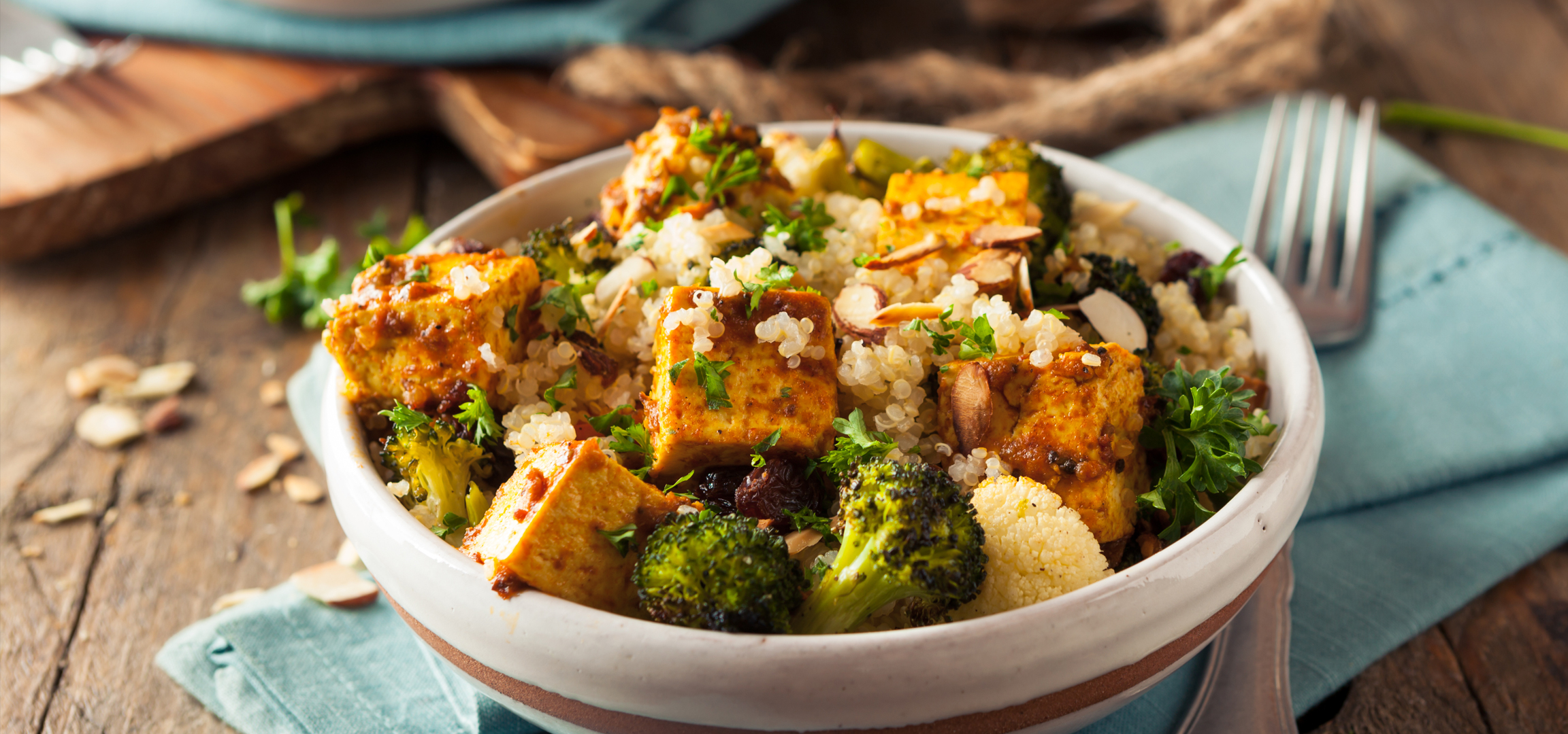 Tofu, brokkoli és quinoa tál mandulával és petrezselyemmel, fa asztalon.