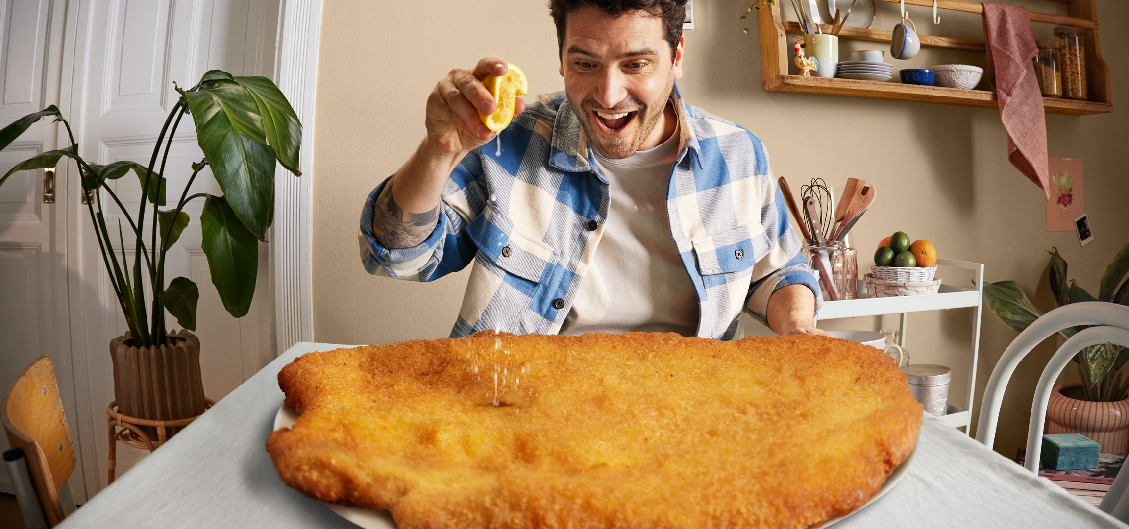 Férfi citromot facsar egy hatalmas rántott húsra, otthoni környezetben.