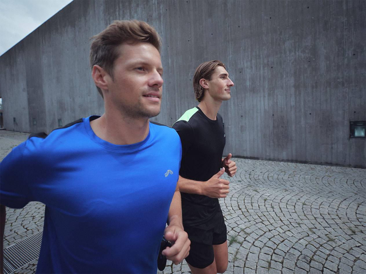 Két férfi fut sportpólóban és rövidnadrágban, az egyik kékben, a másik feketében.