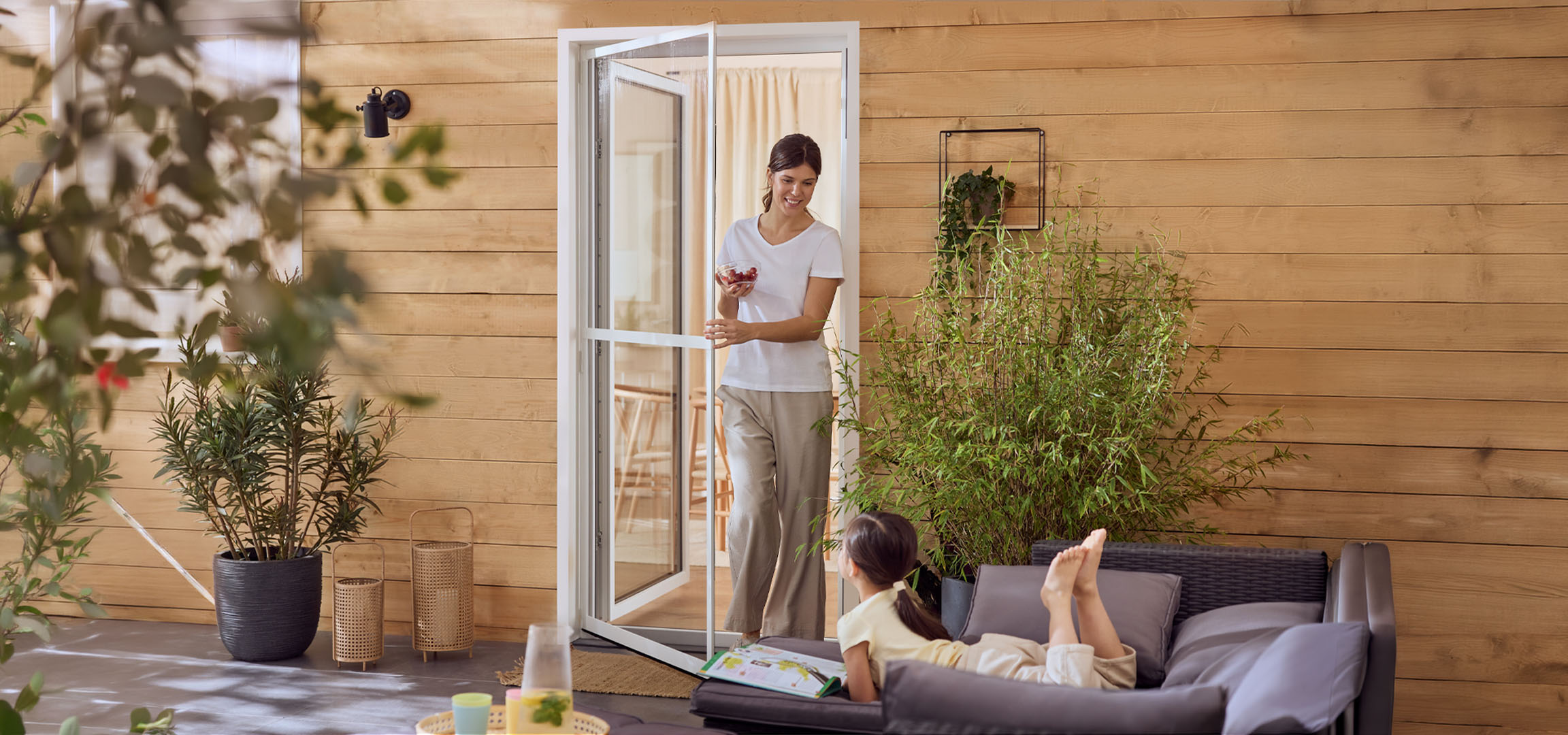 Nő és kislány élvezi a teraszt kerti bútorokkal és növényekkel.