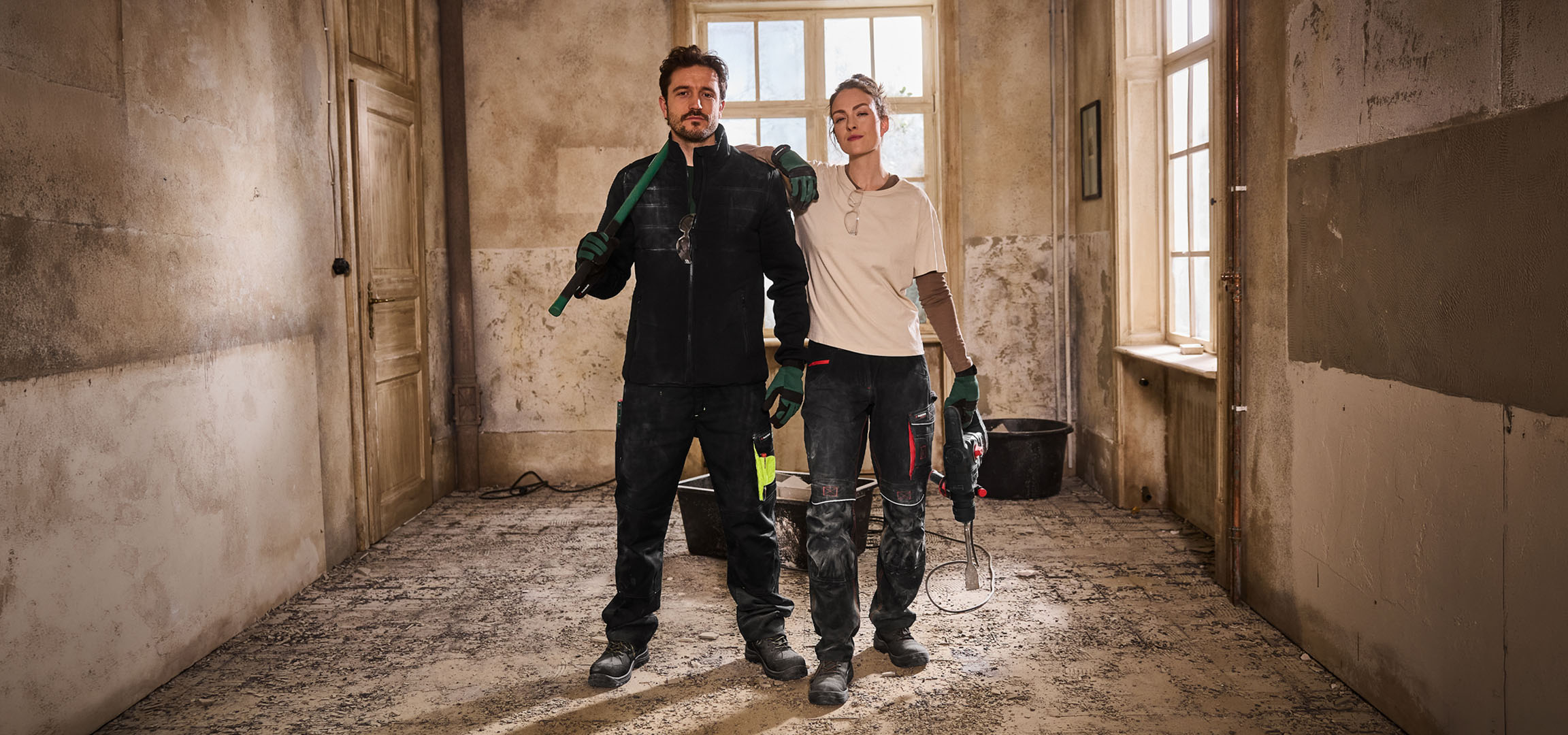 Két építőmunkás munkaruhában szerszámokkal egy építkezésen.