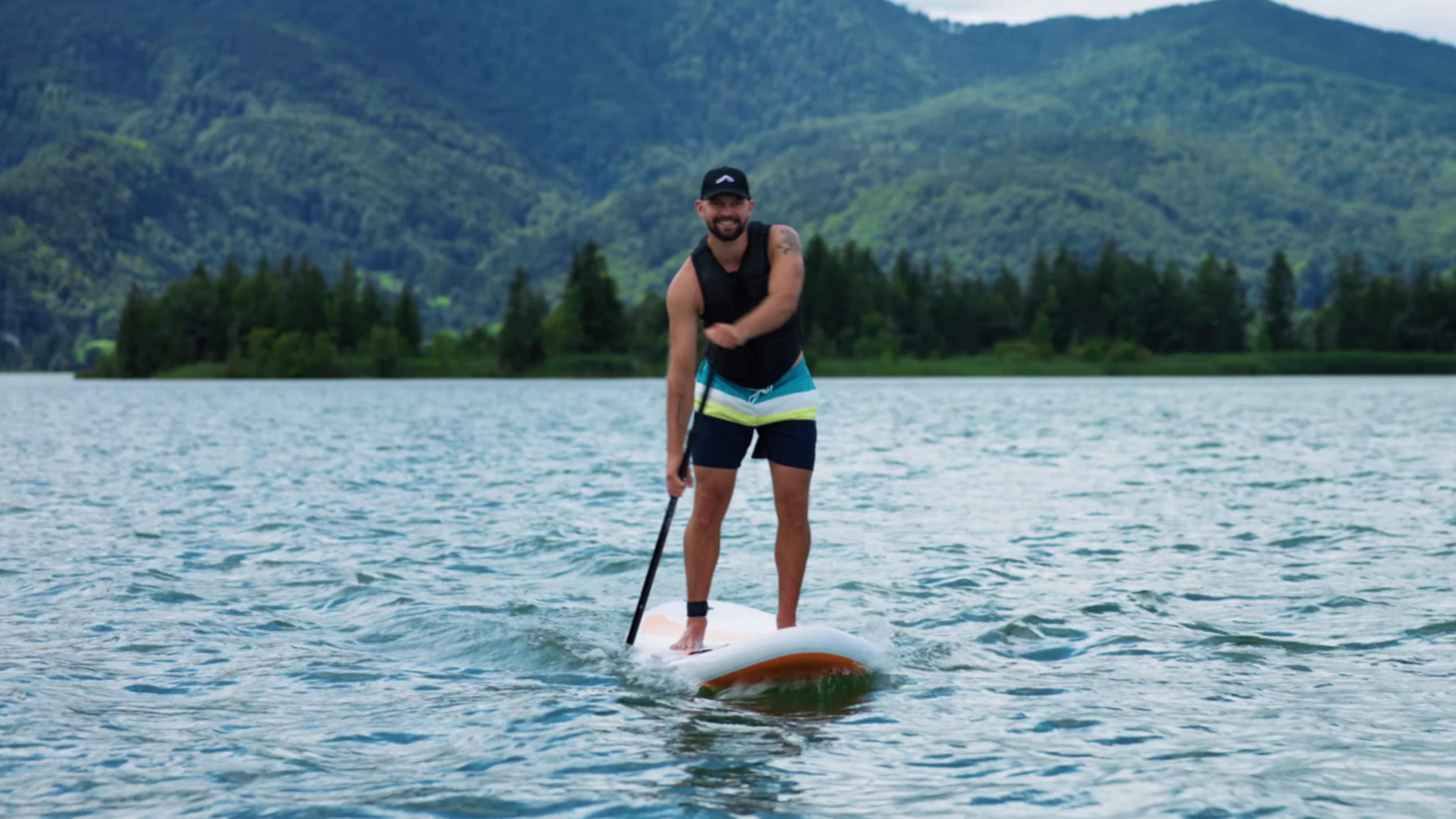 Férfi paddleboardon egy tavon, hegyekkel a háttérben.