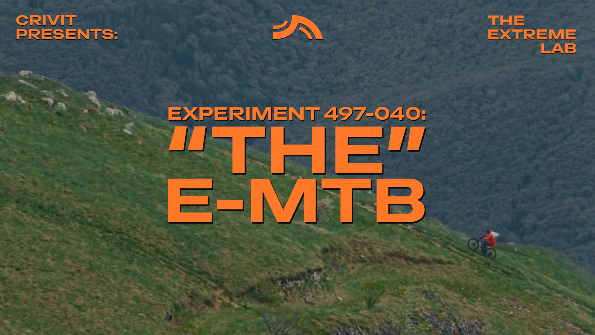 Hegyi kerékpáros füves lejtőn, 'THE E-MTB' és 'THE EXTREME LAB' szöveggel.