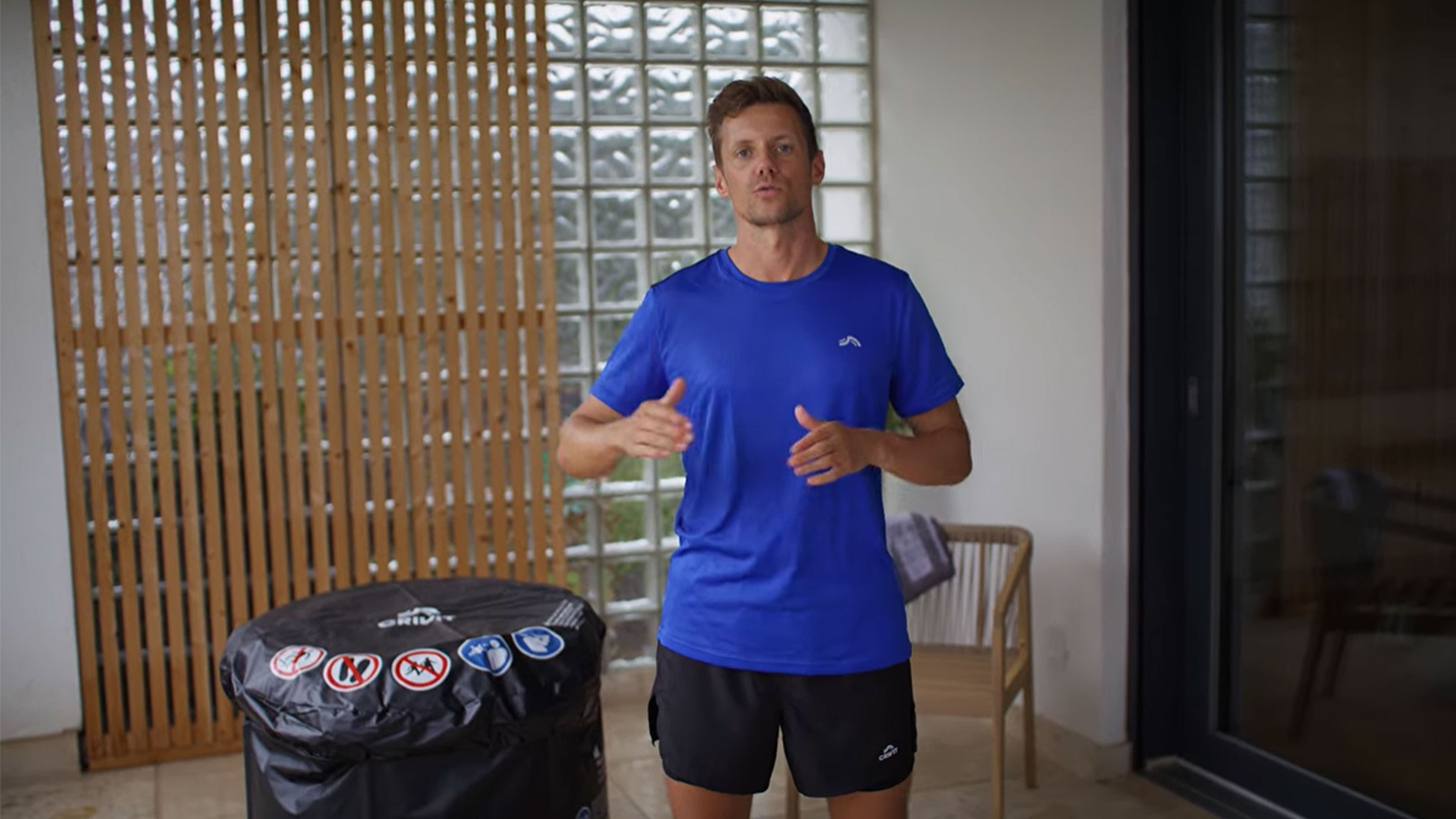 Férfi kék pólóban és fekete rövidnadrágban, fekete pezsgőfürdő-takaró mellett.