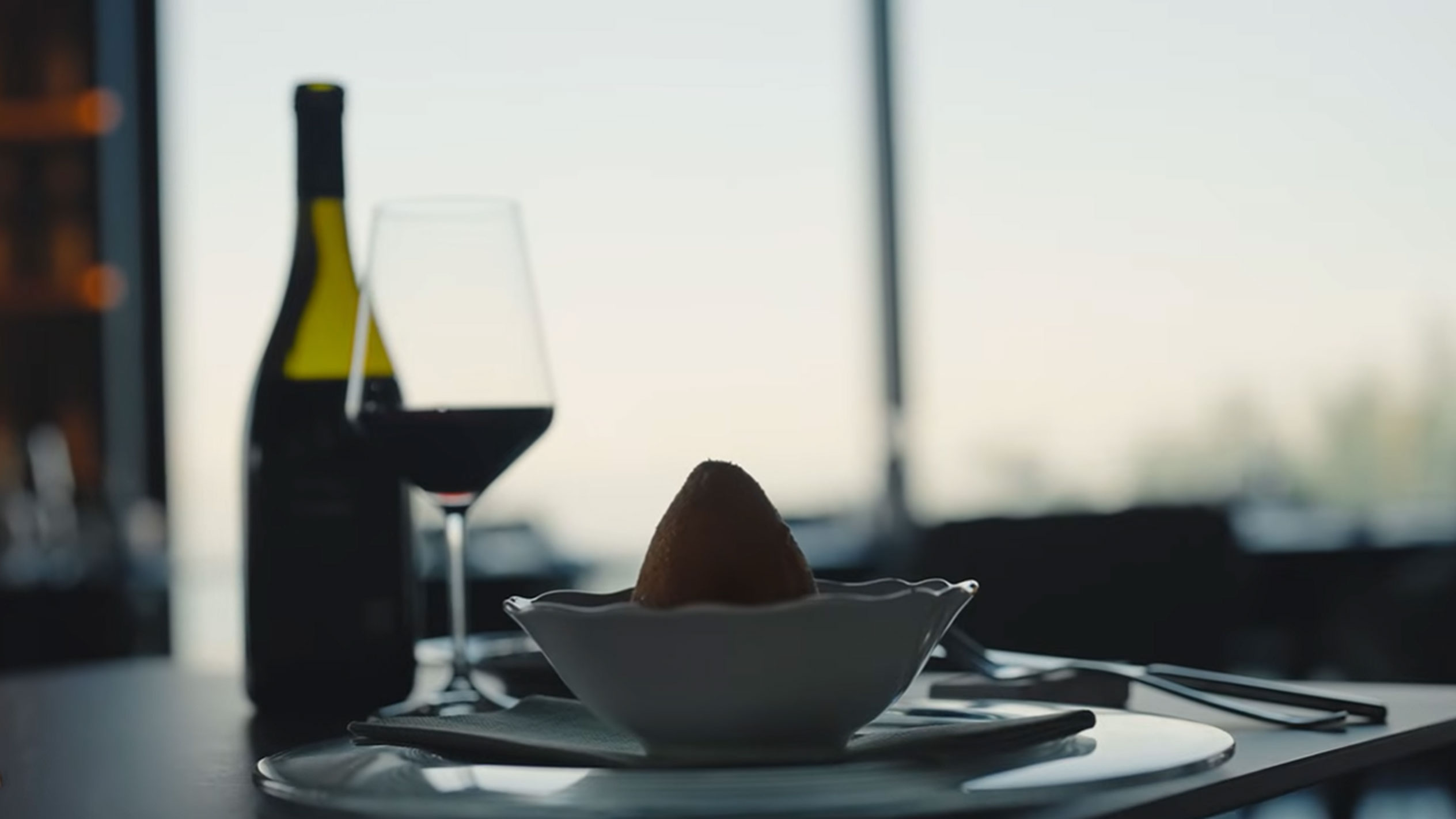 Egy üveg vörösbor és egy pohár egy arancino mellett egy tálban az asztalon.