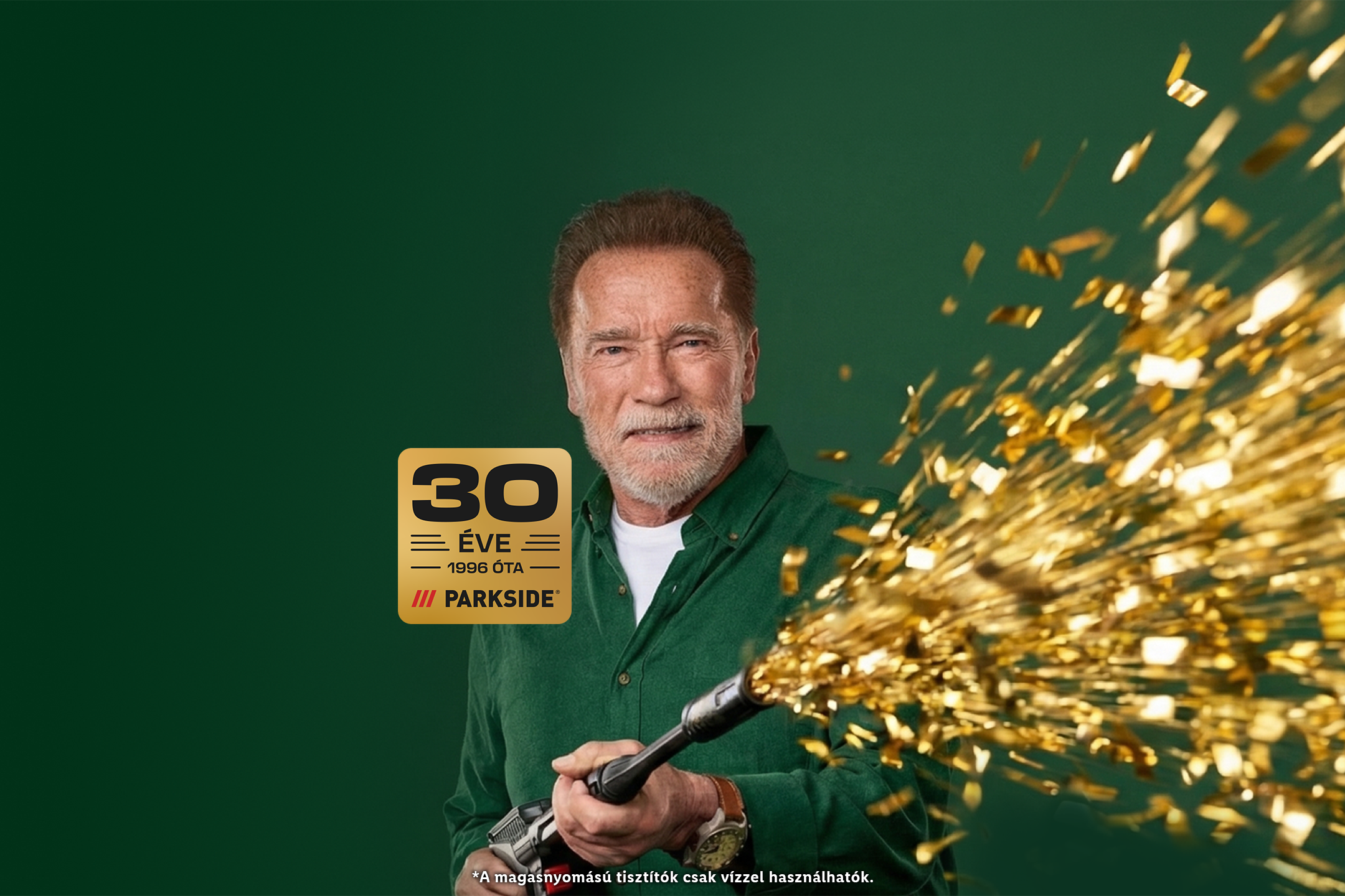 Arnold Schwarzenegger egy zöld háttér előtt áll, kezében egy magasnyomású tisztítóval, amelyből arany konfetti árad, mellette egy 30 éves évfordulós logó.
