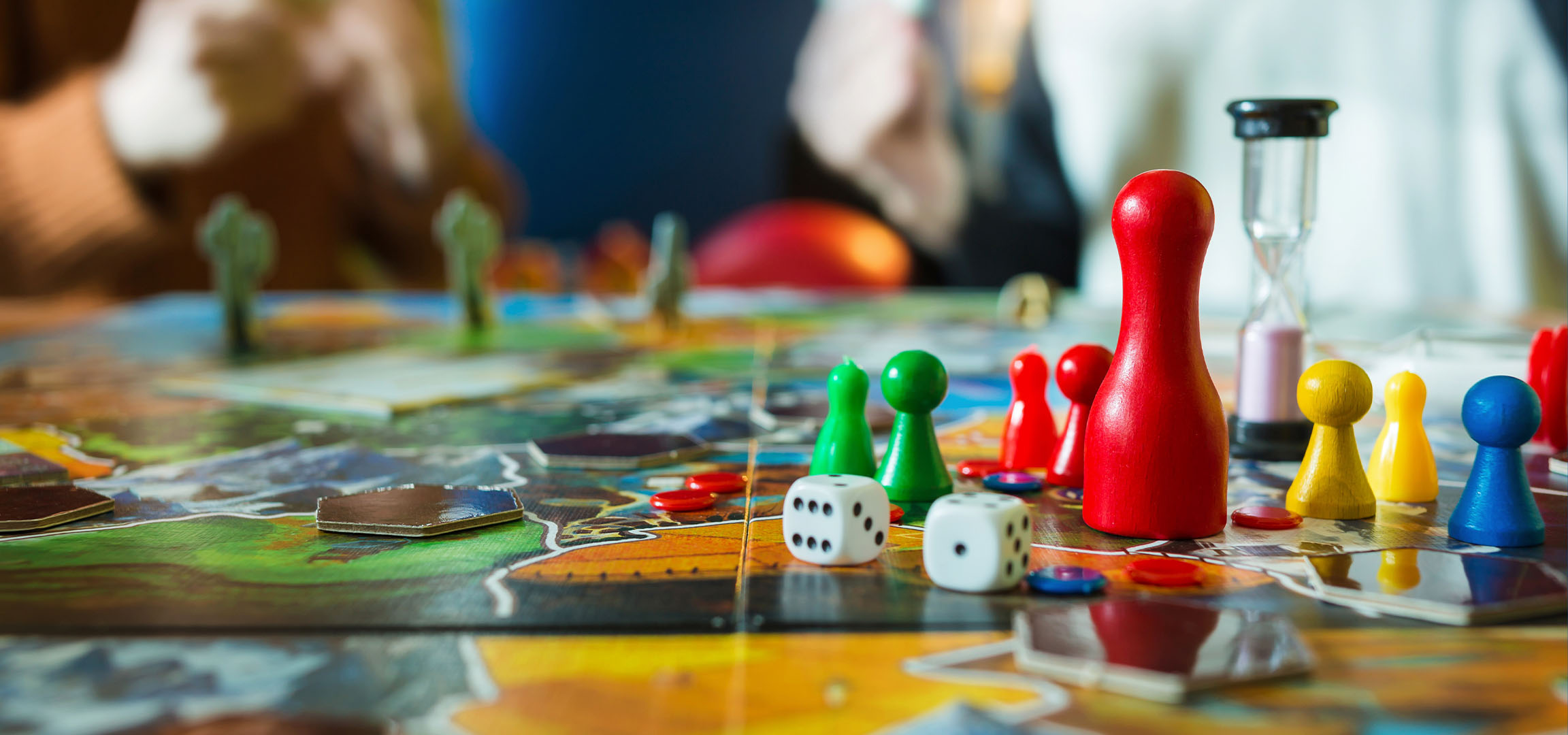 Színes társasjáték figurák, köztük piros, zöld, sárga és kék bábuk, dobókockákkal.