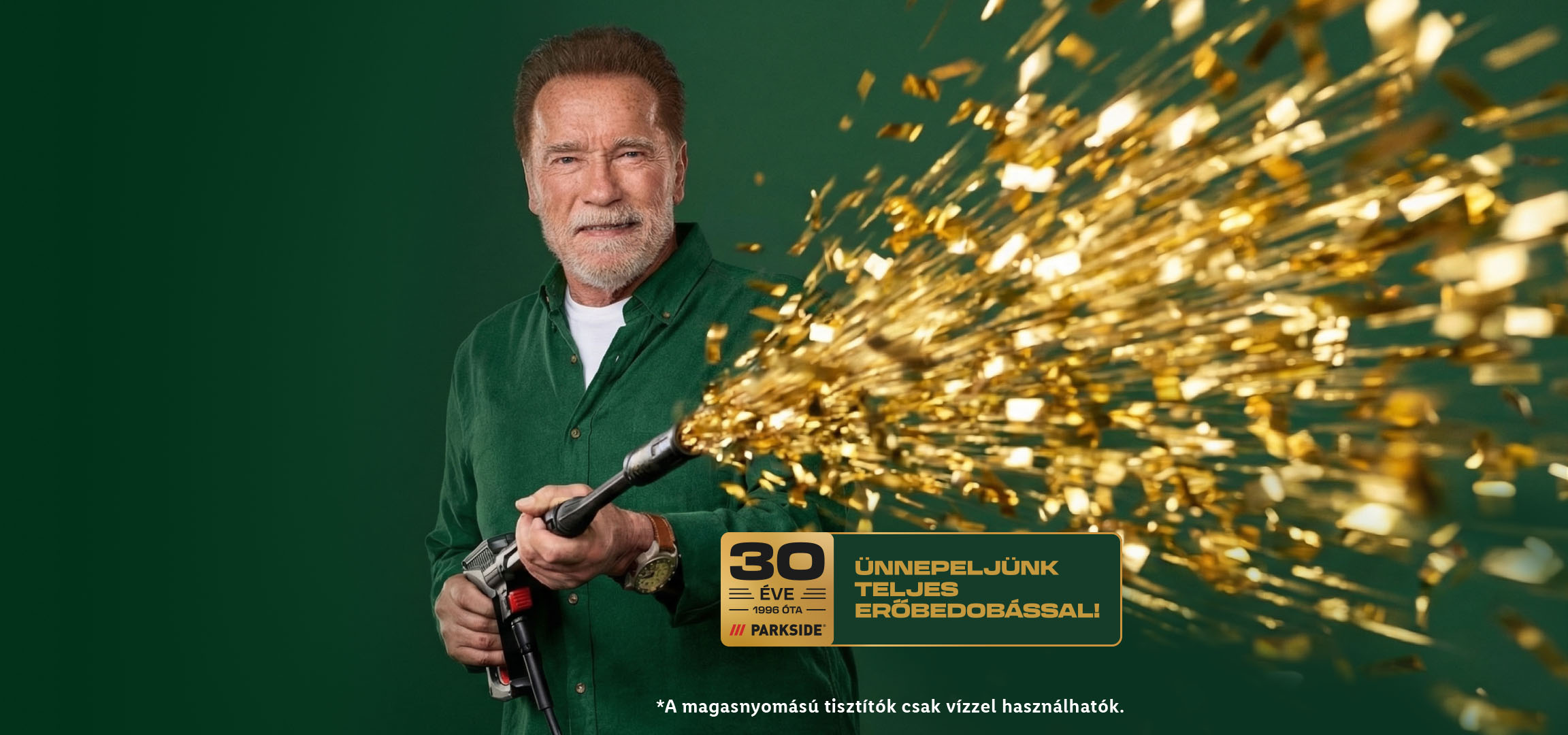 Arnold Schwarzenegger egy magasnyomású tisztítóval arany konfettit fúj, 30 éves évfordulót ünnepelve.