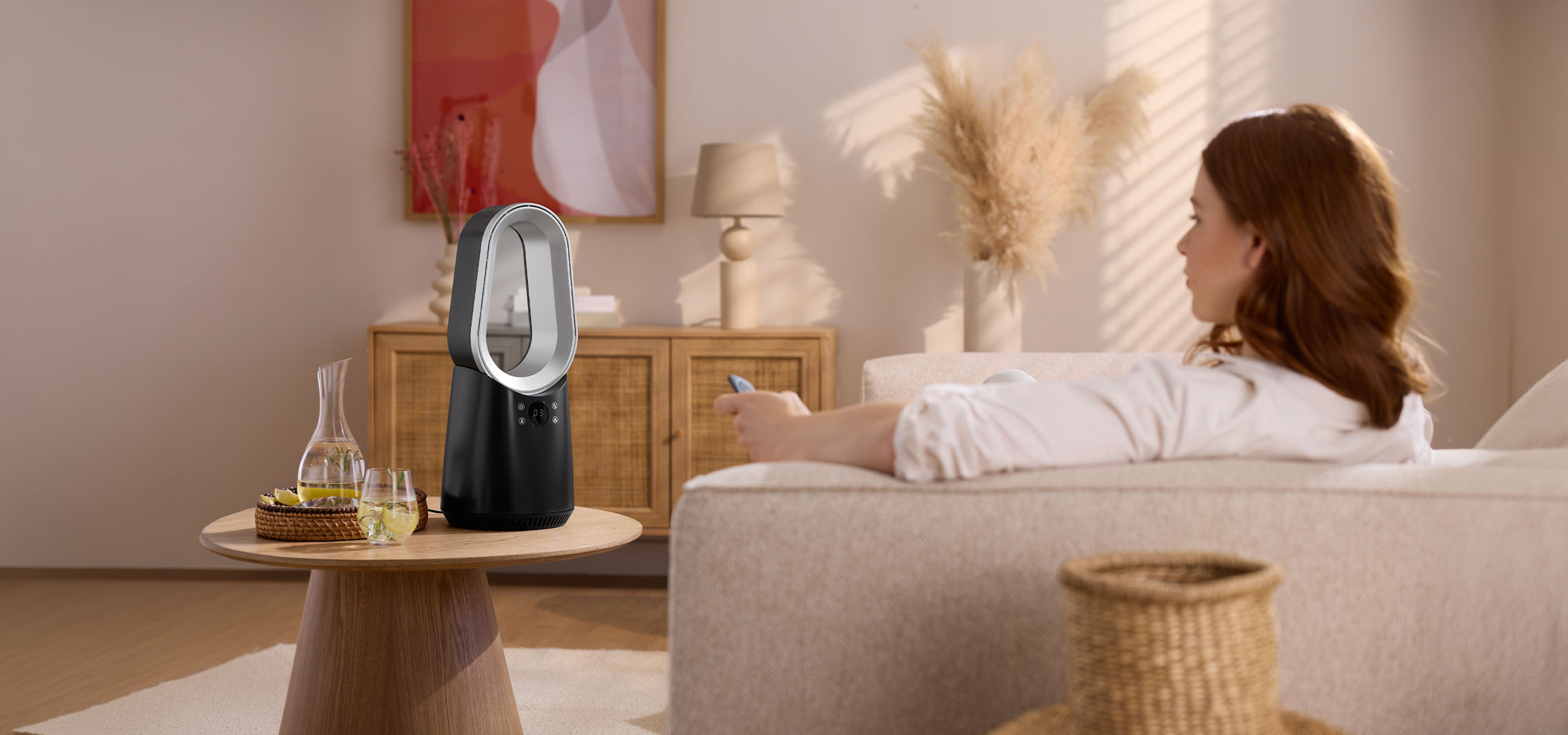 Nő a kanapén távirányítóval, modern ventilátor és italok az asztalon.