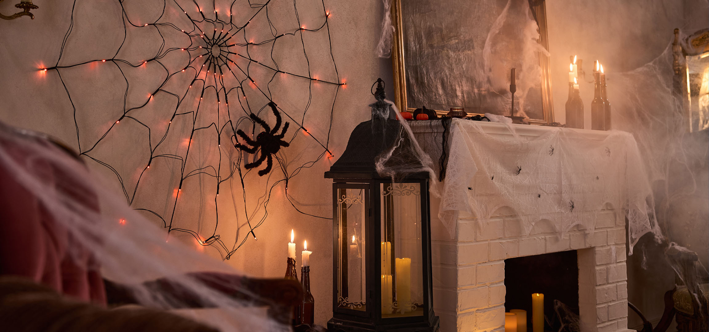 Halloween dekorációk pókháló fényekkel, nagy pókkal és gyertyákkal.