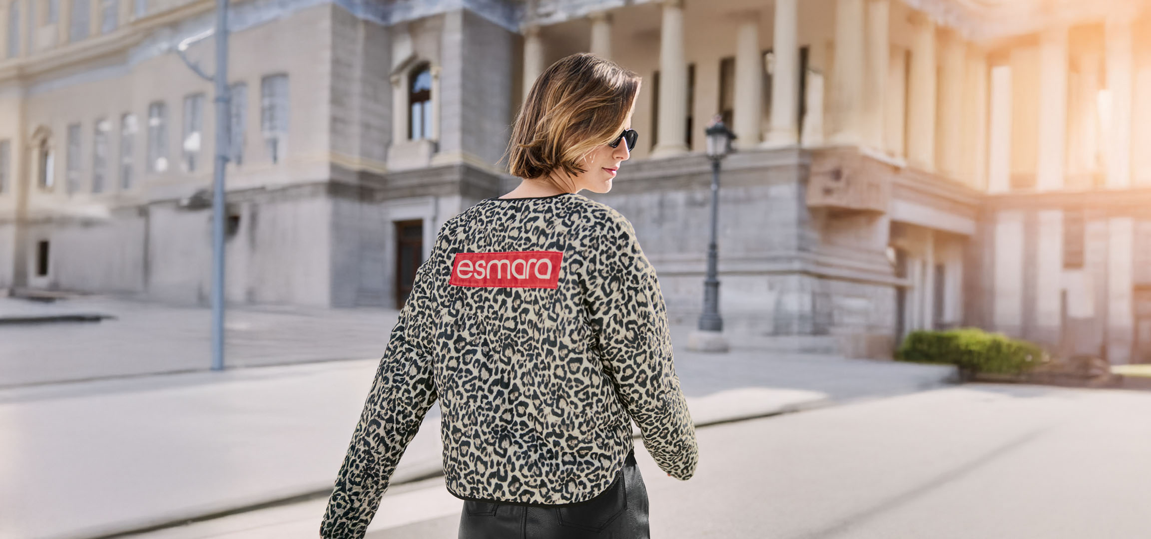 Nő Esmara leopárdmintás kabátban, napszemüvegben, városi utcán.