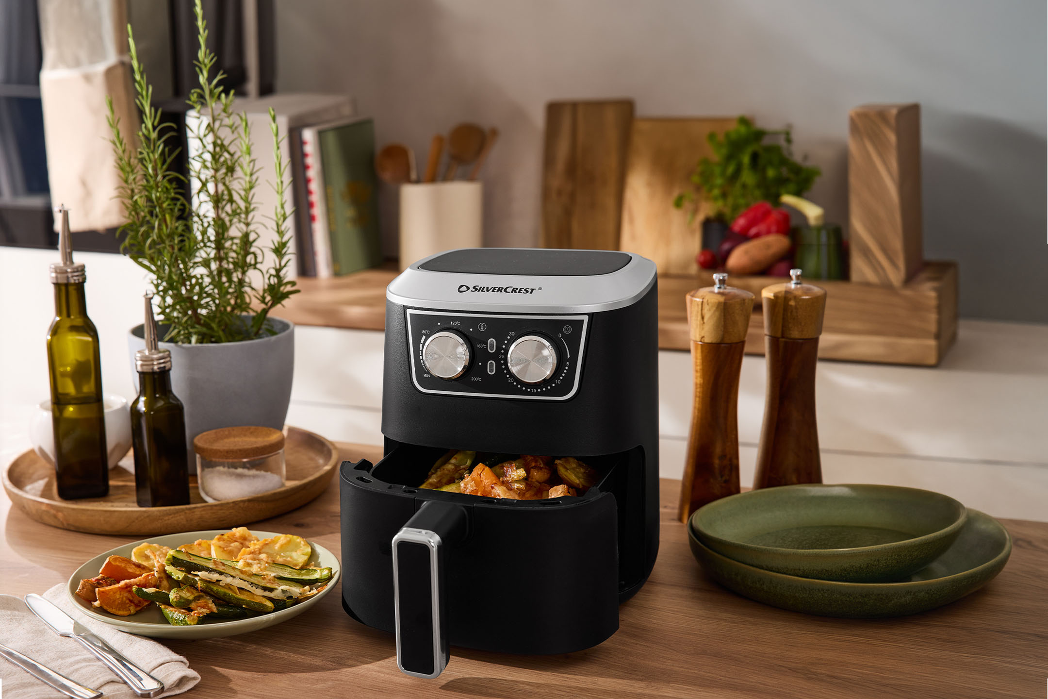 Légkeveréses sütő sült zöldségekkel, olívaolajjal, sóval és borssal egy konyhapulton.