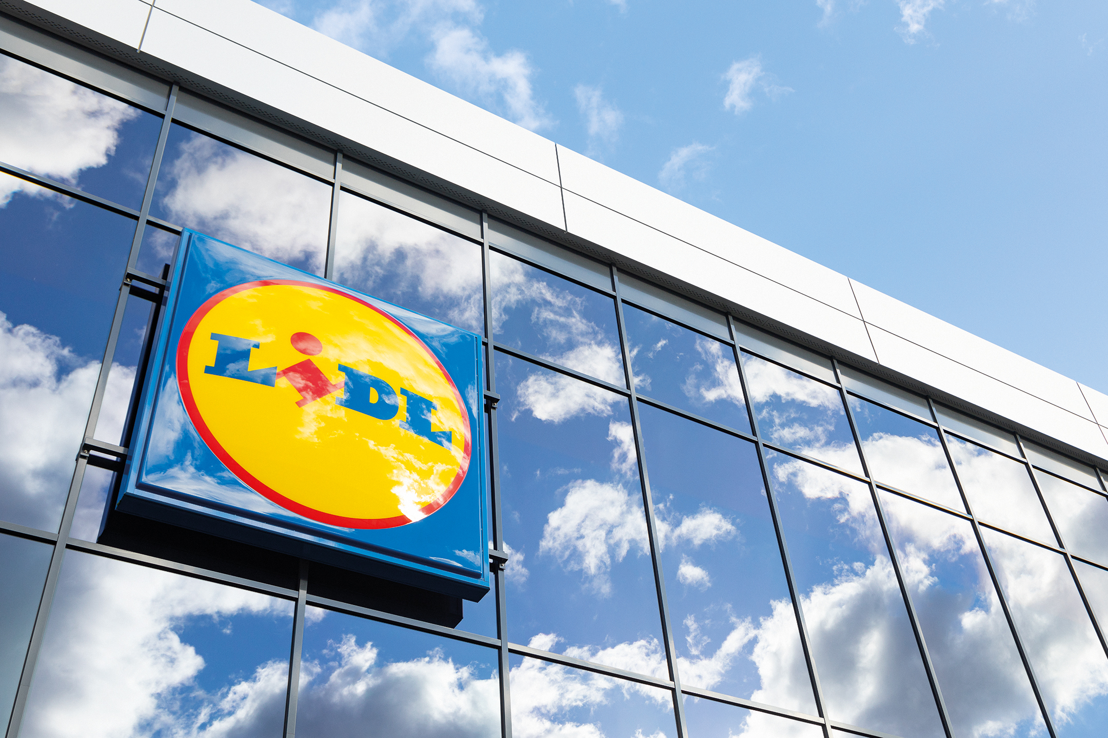 Lidl felirat üveg homlokzaton, ég és felhők tükröződésével.