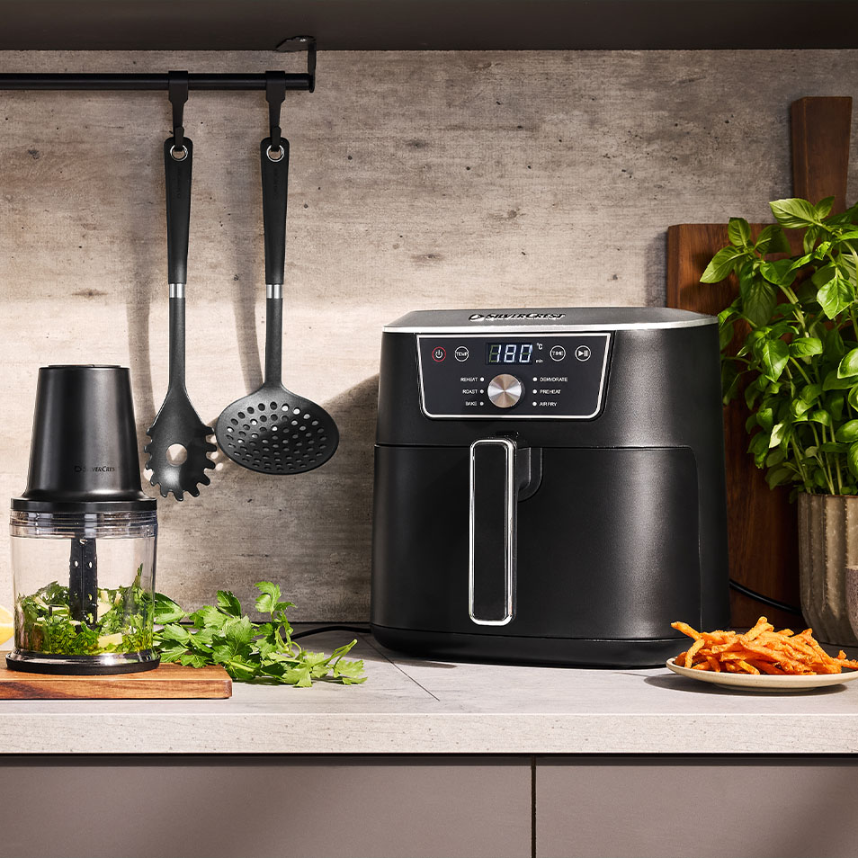 SilverCrest forrólevegős fritőz és aprító konyhapulton friss fűszernövényekkel és édesburgonya hasábburgonyával.