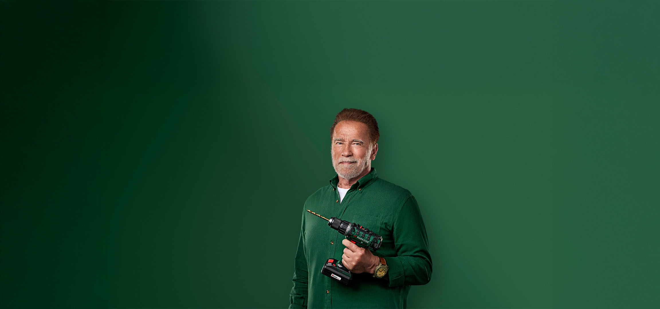 Arnold Schwarzenegger Parkside fúrót tart zöld háttér előtt.