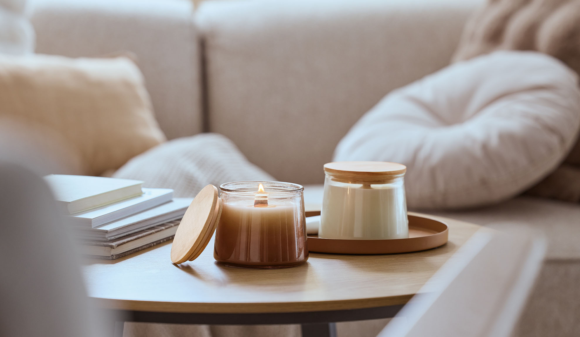 Két illatgyertya egy fa asztalon, az egyik ég, a háttérben egy hangulatos kanapé.