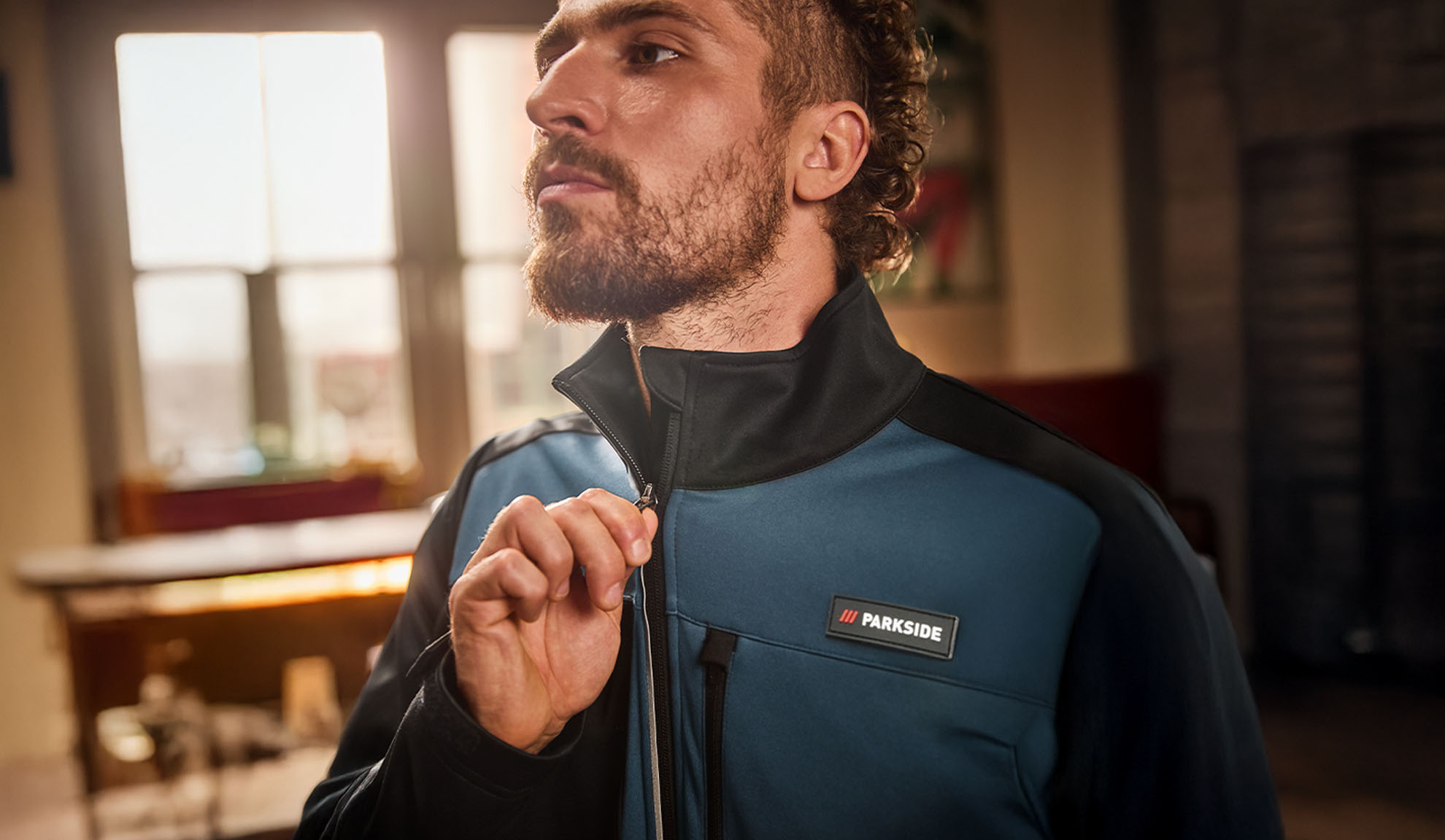 Férfi kék és fekete Parkside munkakabátban, éppen felhúzza a cipzárt.