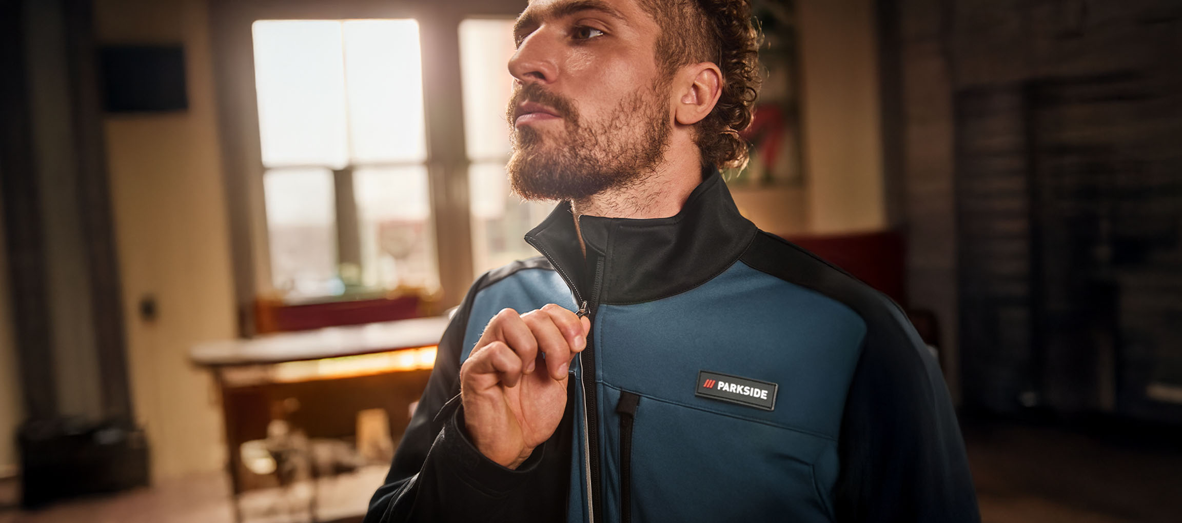 Férfi kék és fekete Parkside munkakabátban, éppen felhúzza a cipzárt