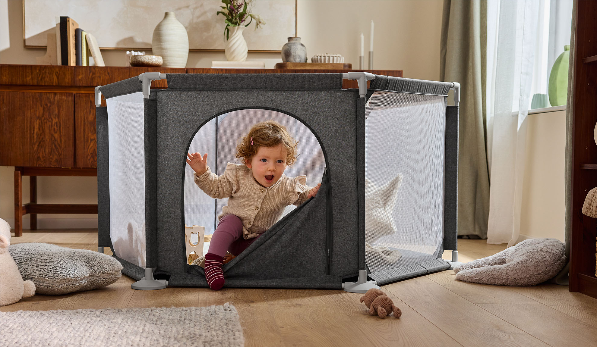 Boldog baba mászik ki egy szürke járókából egy hangulatos nappaliban.