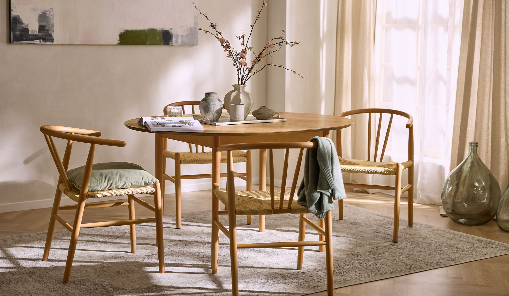 Világos étkező kerek fa asztallal, fa székekkel kötélülésekkel és virágdíszítéssel.