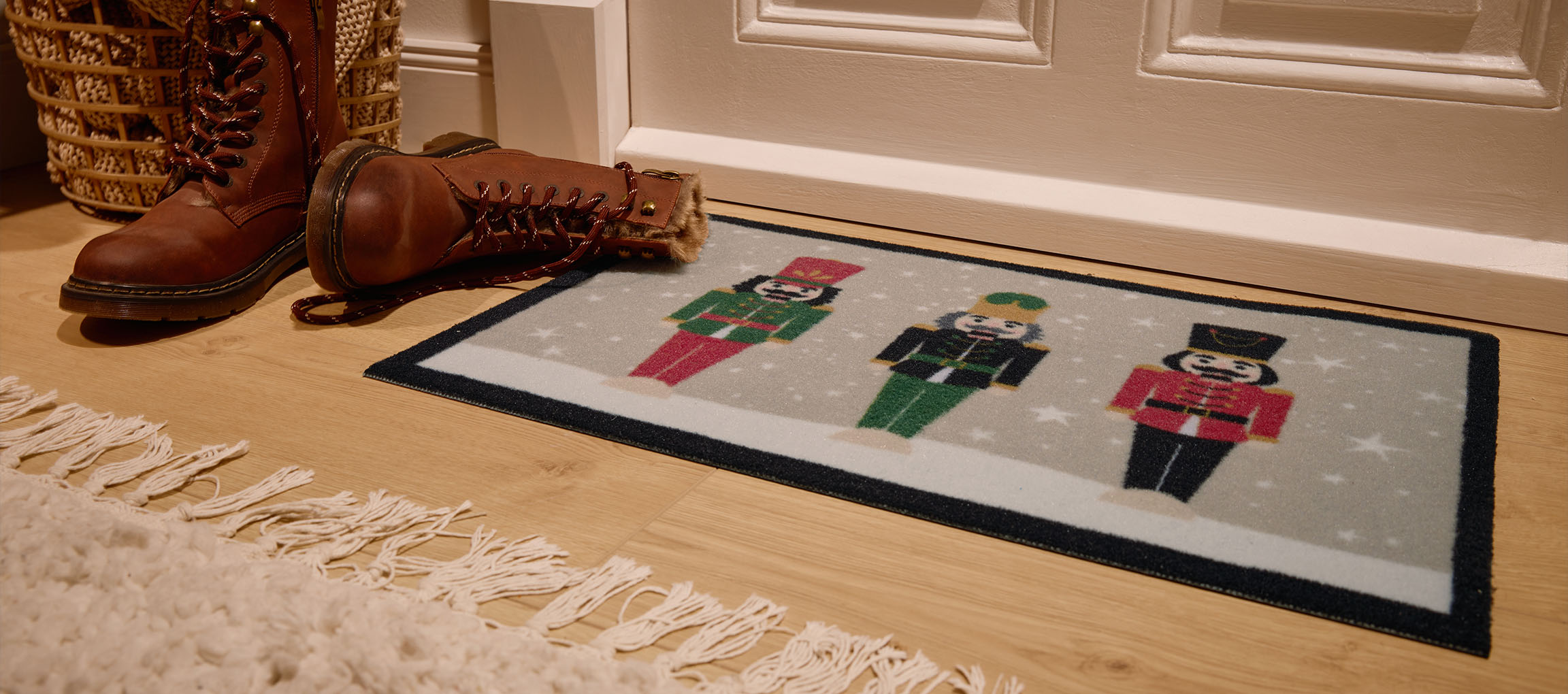Karácsonyi diótörő lábtörlő, barna csizmák és fonott kosár a bejáratnál.