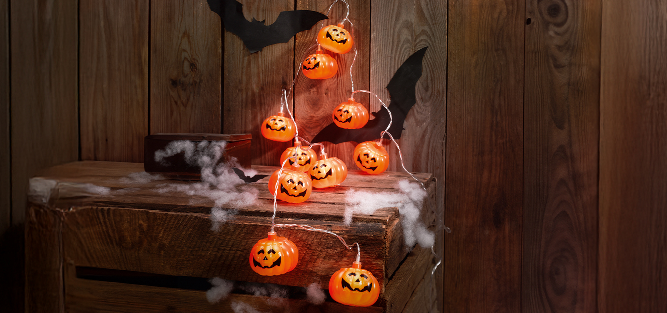 Halloween töklámpás füzér és denevér dekoráció egy fa ládán, pókhálóval.