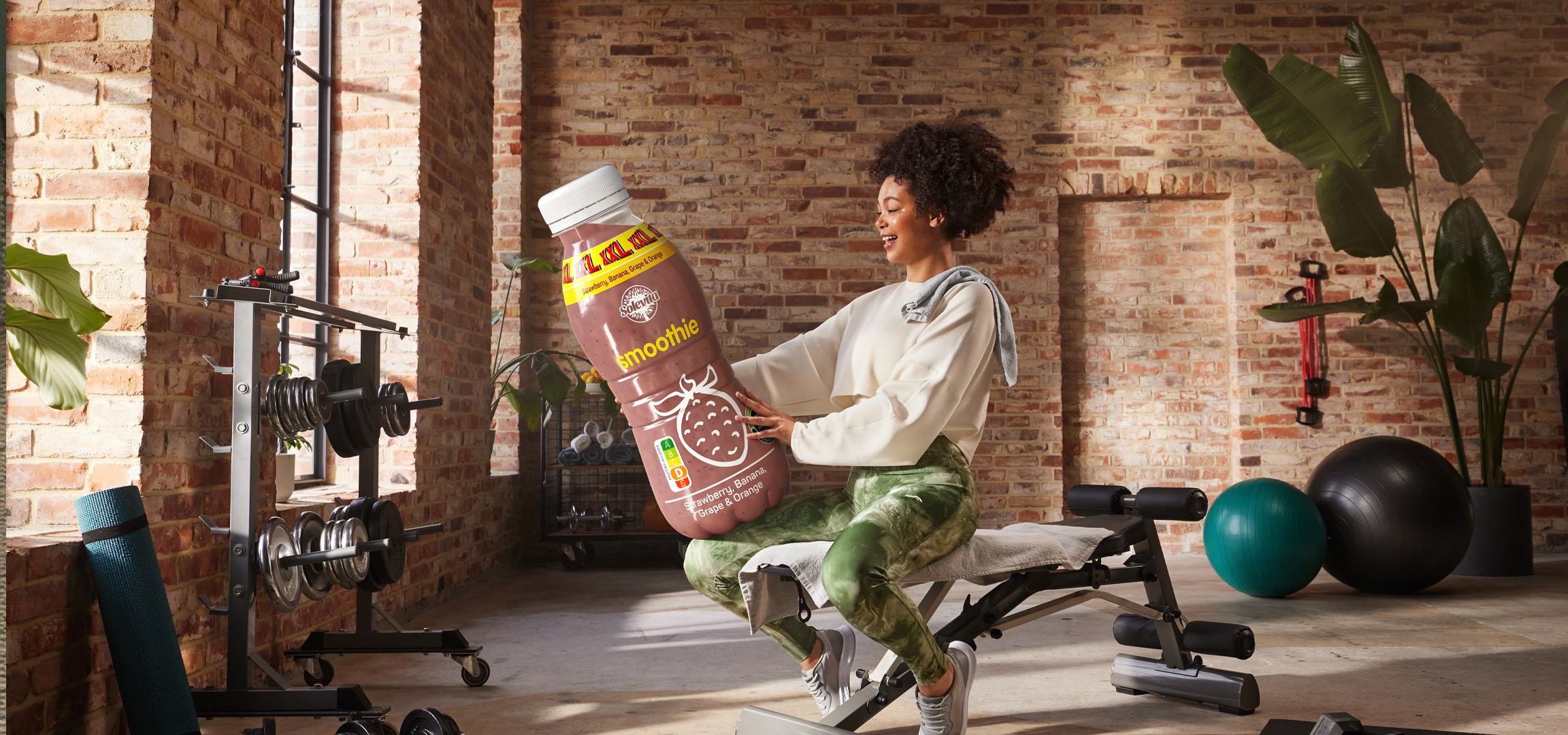 Nő tart egy nagy SoleVita smoothie-t egy edzőteremben.