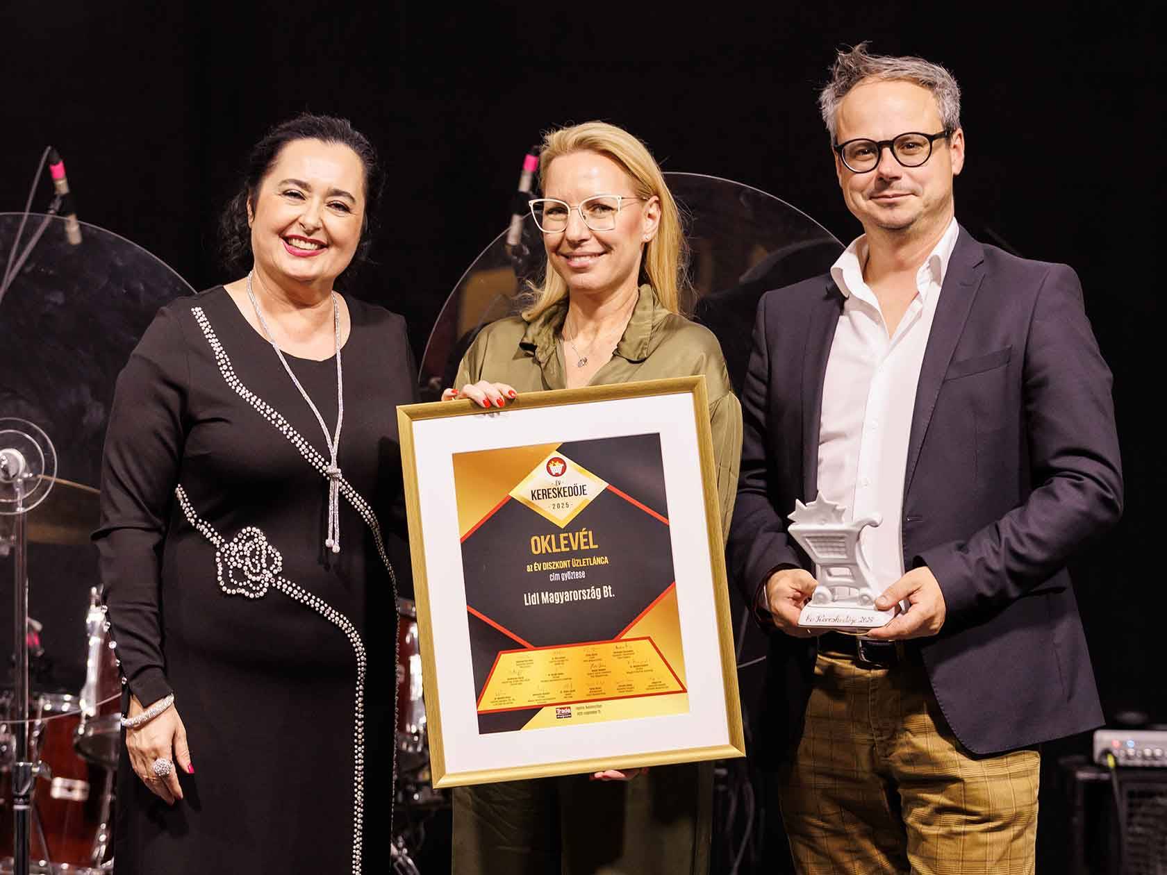 Három ember tartja a „Kereskedője 2025” oklevelet, amely a Lidl Hungarianország Bt.-t az év diszkont üzletláncának nevezi.