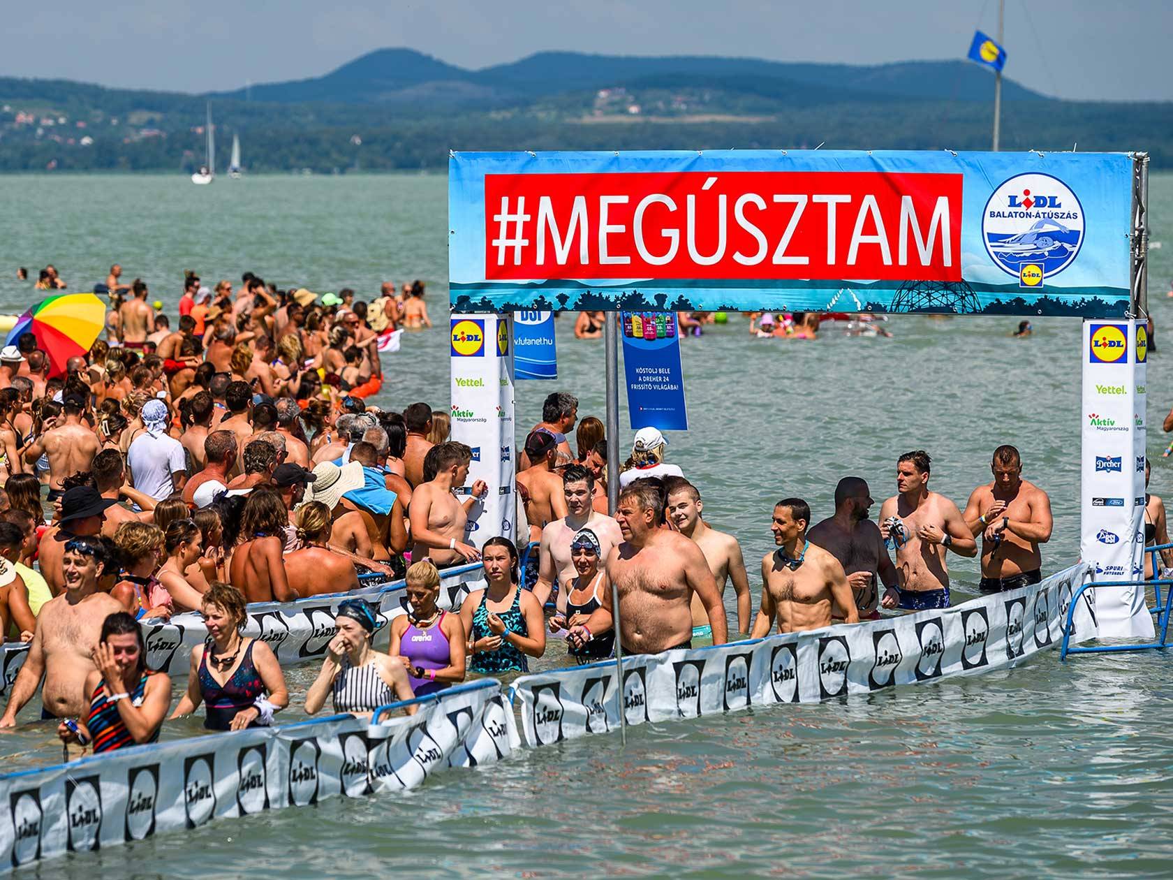 A Lidl Balaton-átúszás versenyzői a vízben, a #MEGÚSZTAM feliratú molinó előtt.