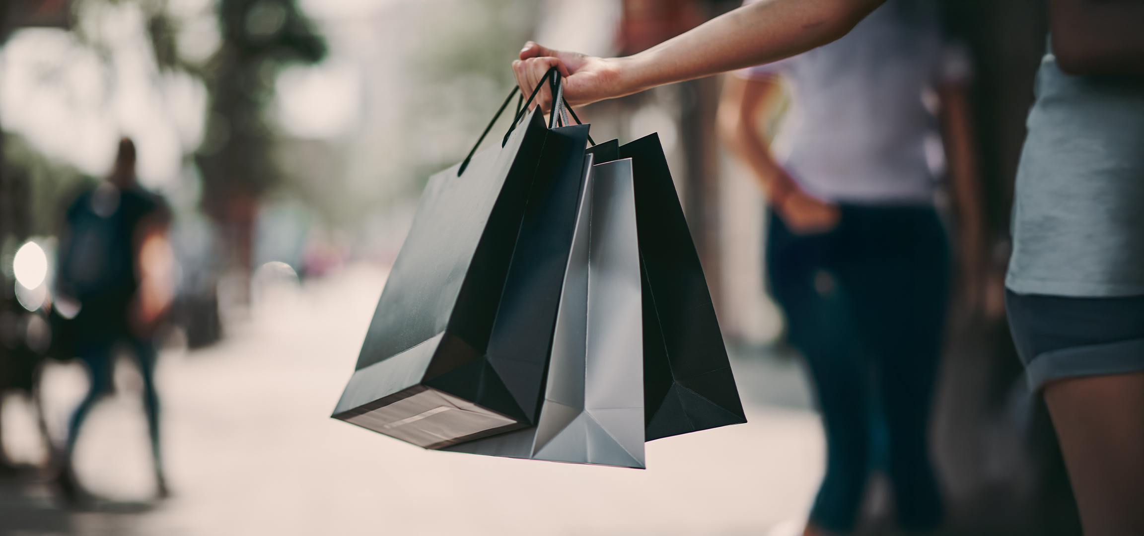 Fekete bevásárlótáskák egy személy kezében, városi környezetben.