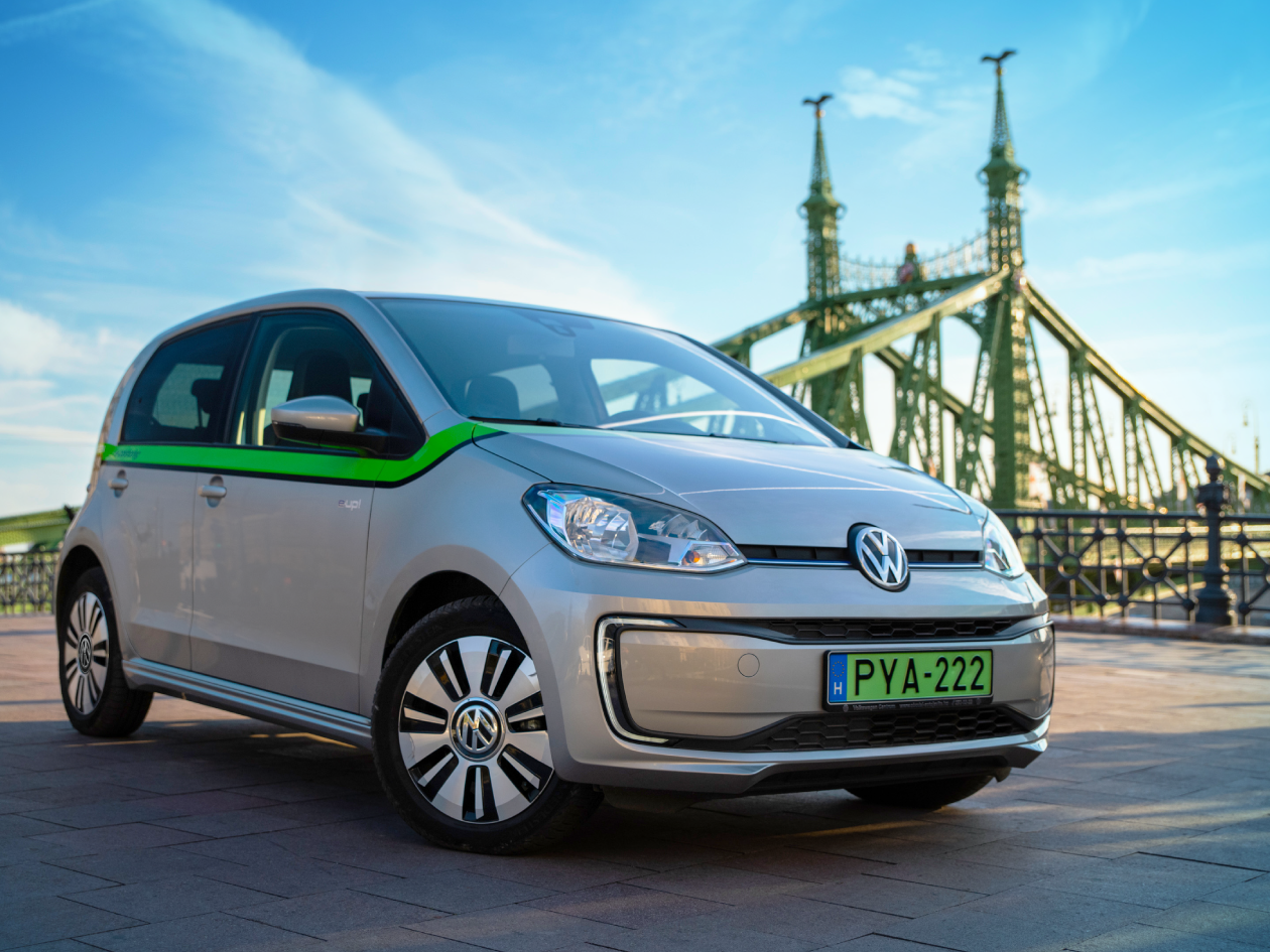 Ezüstszínű Volkswagen e-Up! autó zöld csíkkal, háttérben a Szabadság híddal.
