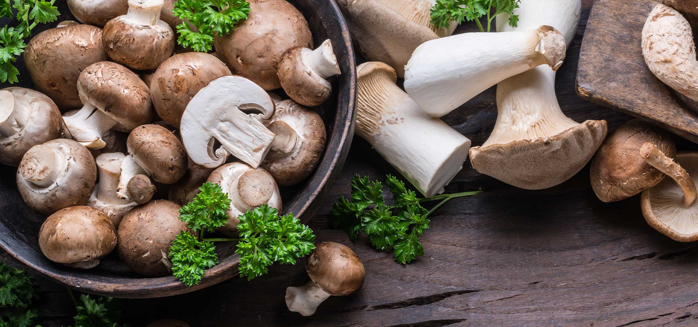 Különböző gombafajták, köztük csiperke, laskagomba és shiitake, petrezselyemmel díszítve.
