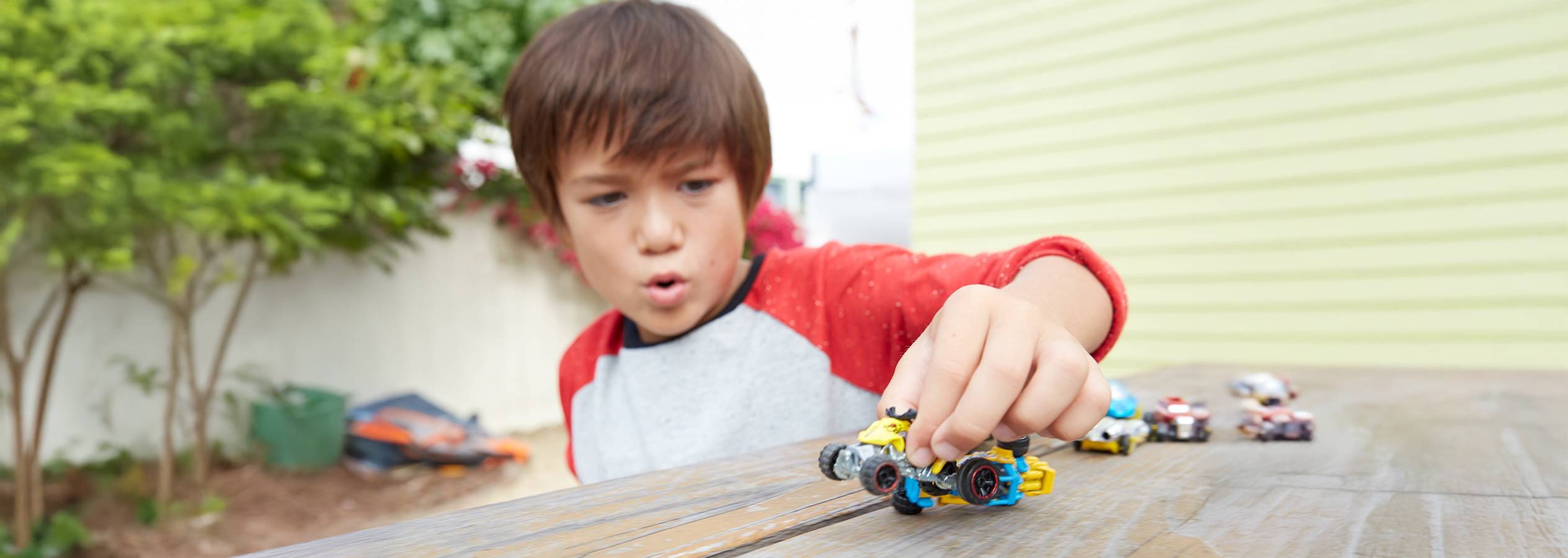Egy fiú játszik egy sárga Hot Wheels kisautóval egy fa asztalon.
