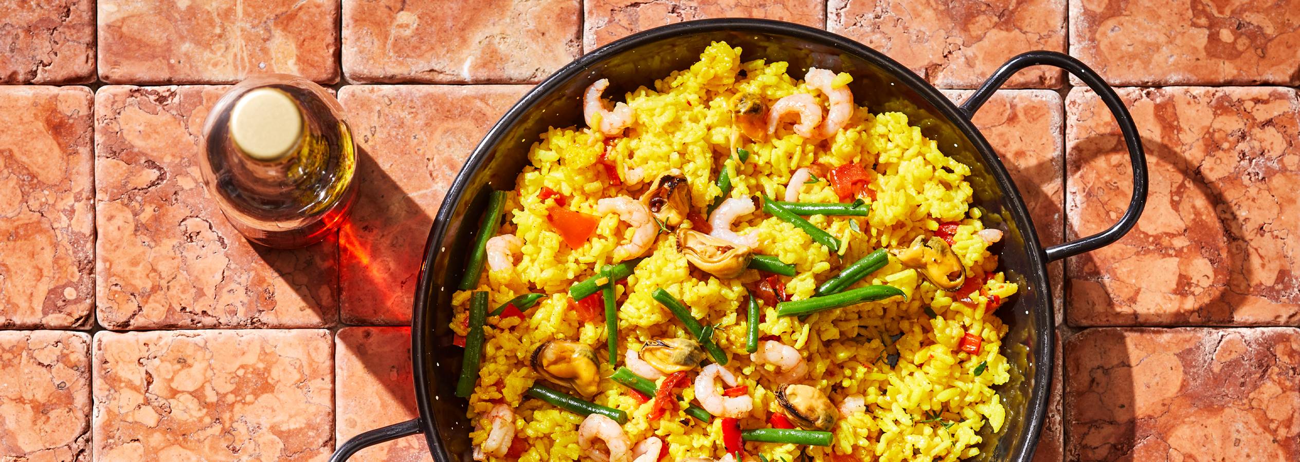 Paella serpenyőben, garnélával, kagylóval és zöldbabbal, olajjal egy üvegben.