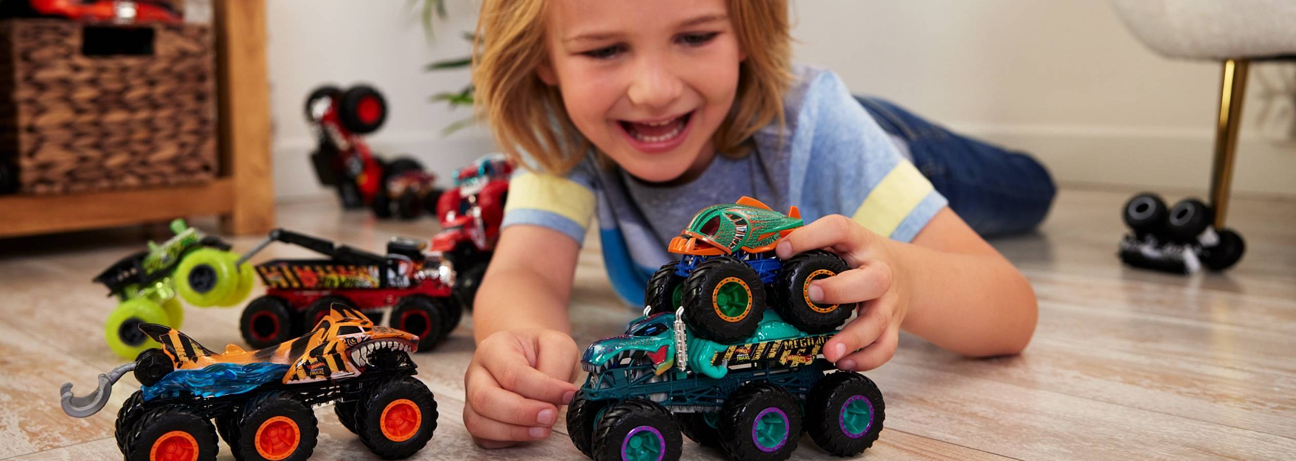 Egy kisfiú Hot Wheels Monster Trucks játékautókkal játszik a földön.