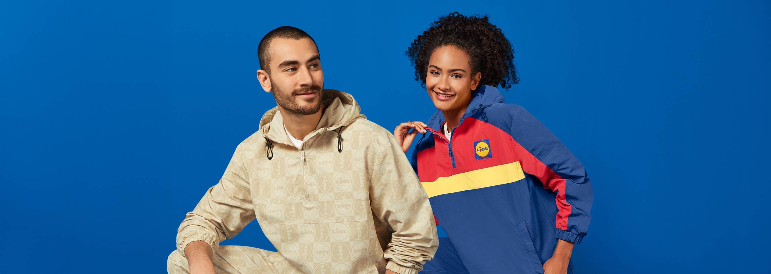 Két fiatal felnőtt Lidl márkájú dzsekikben pózol egy kék háttér előtt.