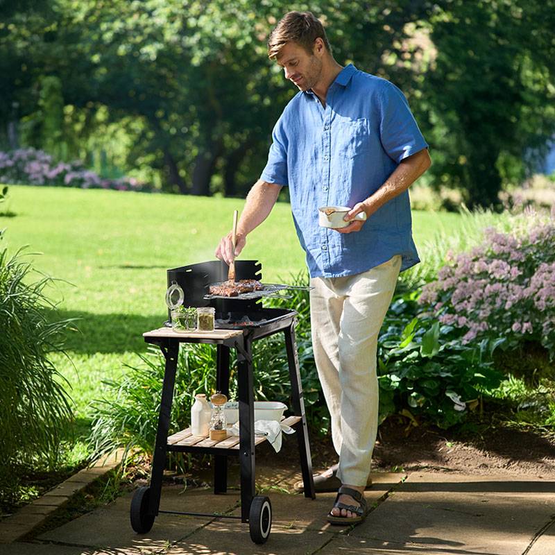 Férfi grillez steaket egy kerti grillen.